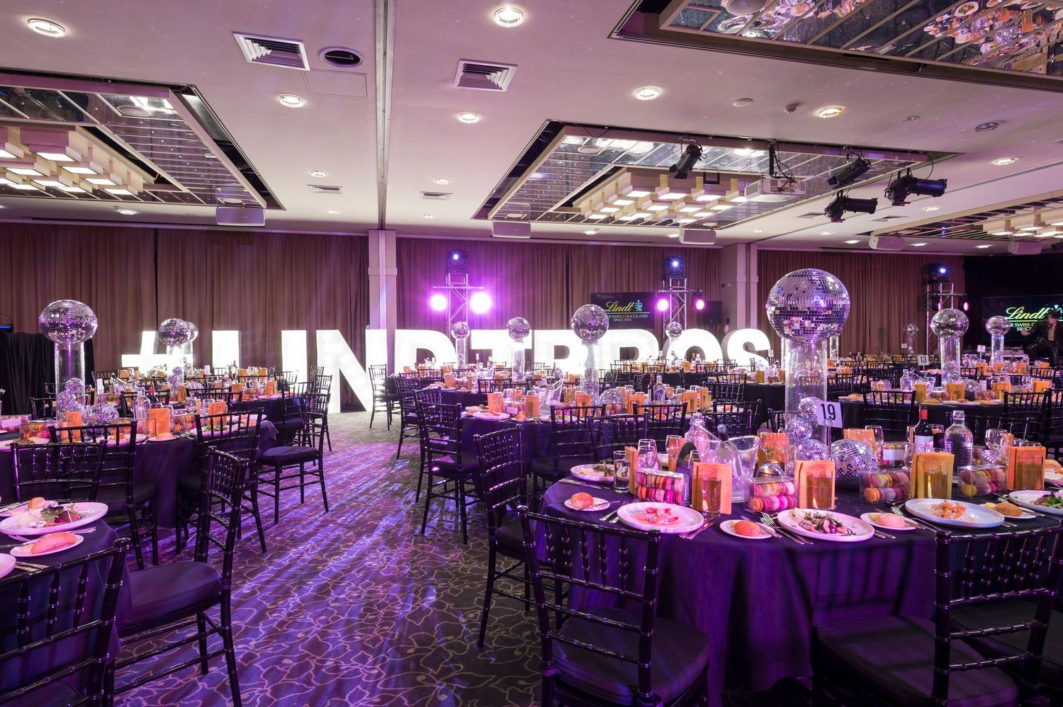 Elegant ballroom decorated in purple lighting with round tables, chiavari chairs and illuminated centerpieces for formal event.