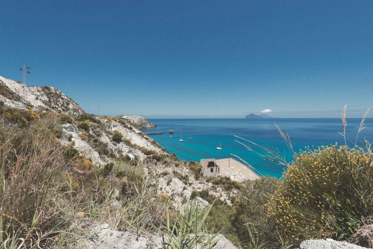 Panoramic coastal view showing rugged cliffs and turquoise ocean waters under bright blue skies.