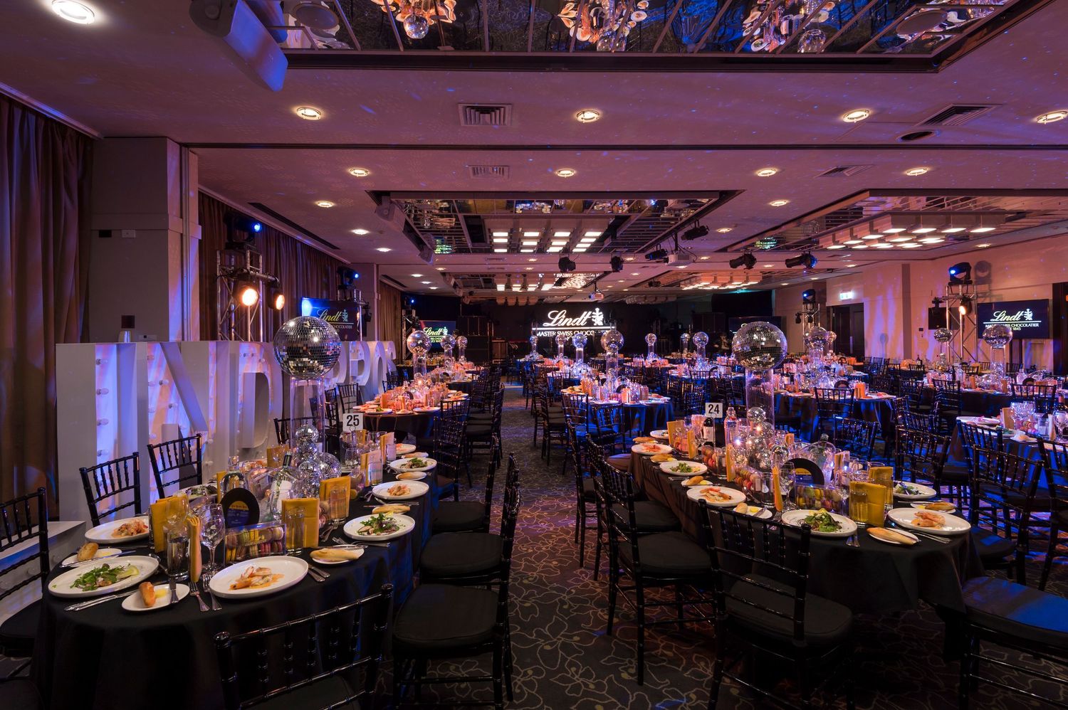 Elegant banquet hall with purple ambient lighting, round tables, and decorative ceiling features for special events.