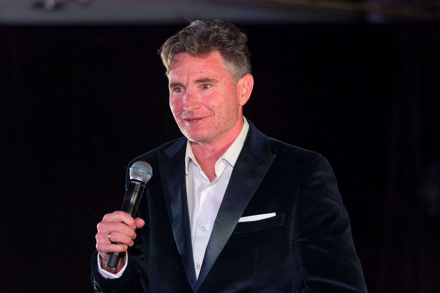 A series of black and white photos showing a speaker in a dark suit holding a microphone at various angles.