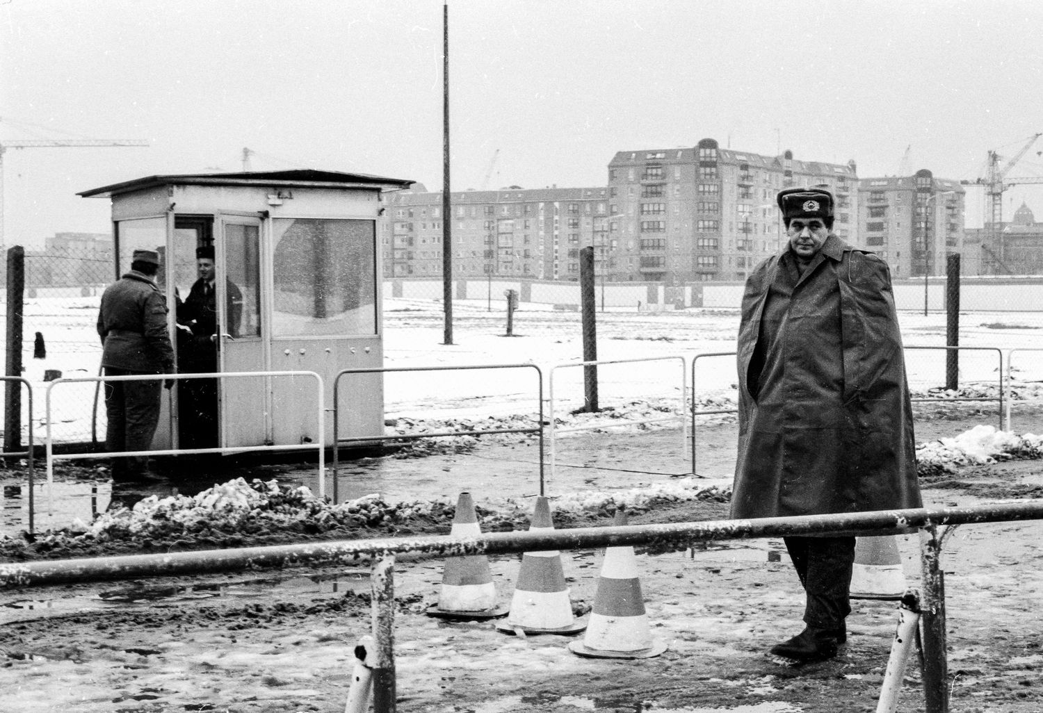 Black and white photo strip showing figures standing in a snowy urban landscape with buildings in the distance.