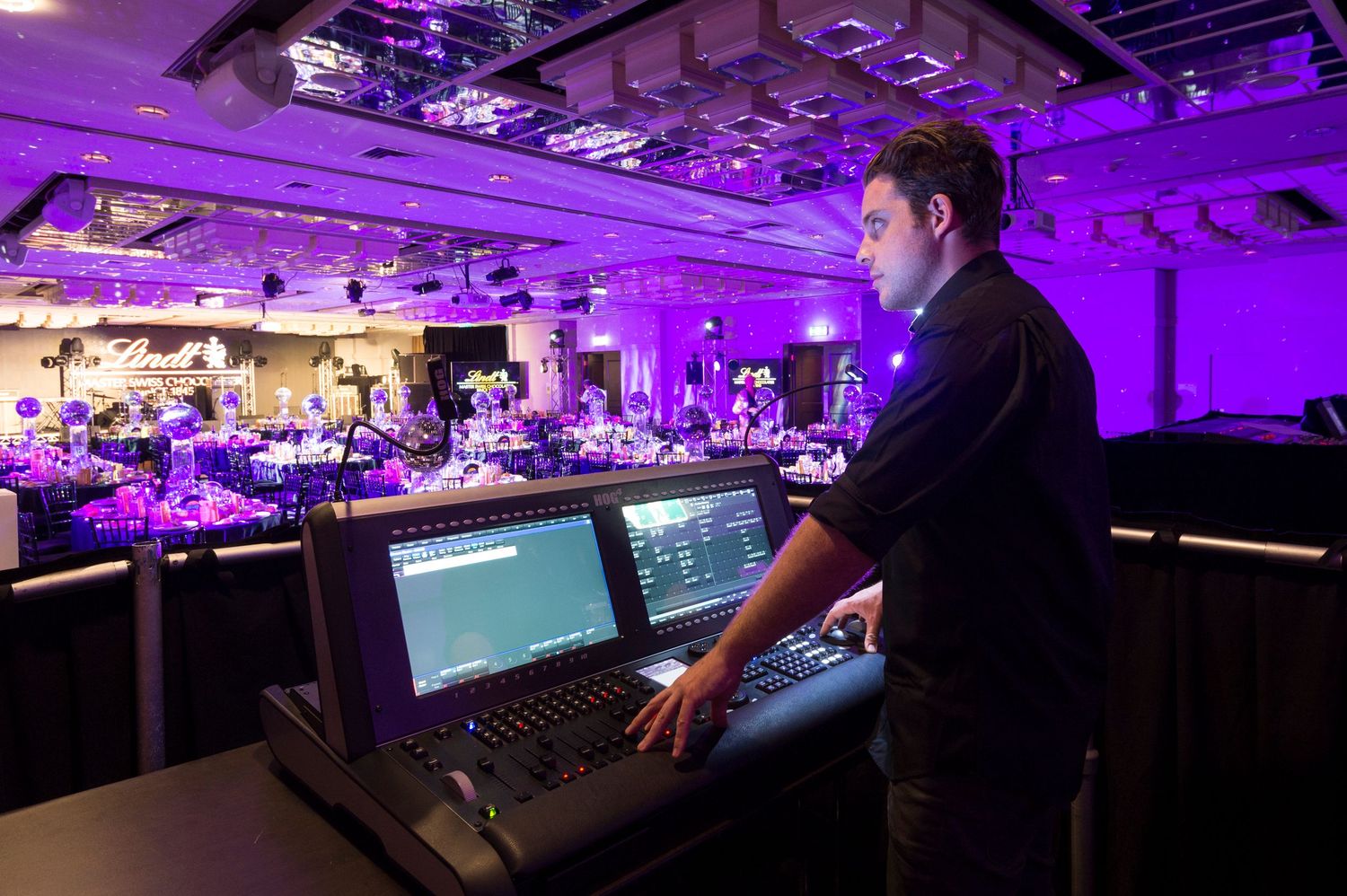 Esports tournament venue illuminated in purple lighting with multiple gaming stations and large display screens.