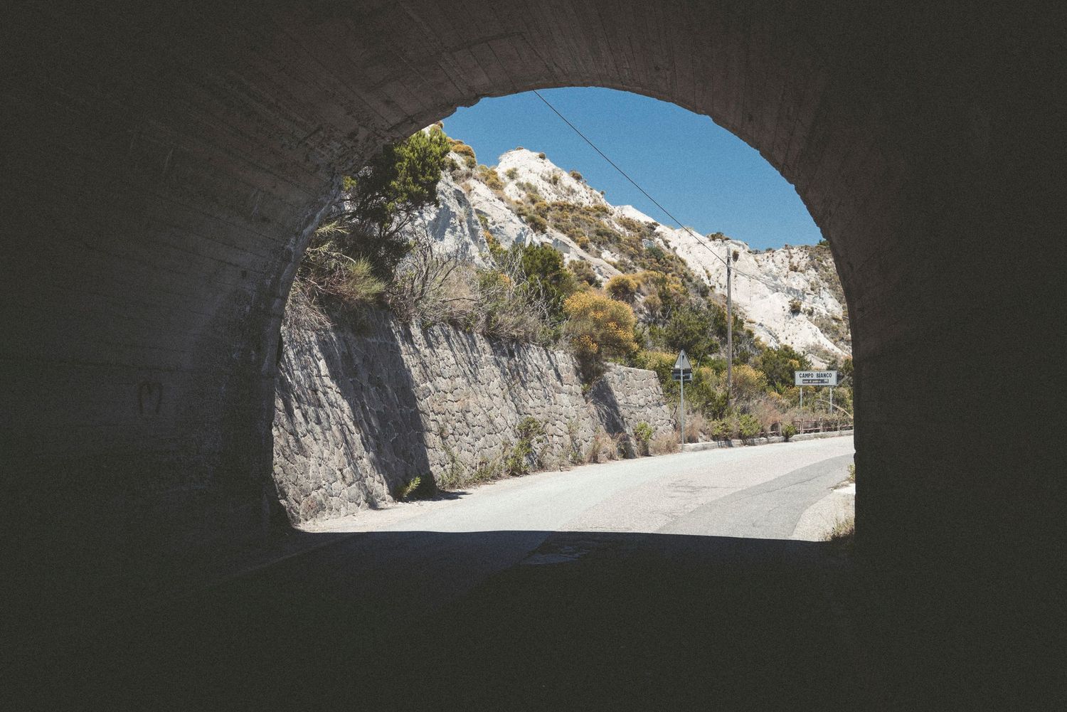 Dramatic rocky cliffs and mountainous terrain line a winding road through a scenic mountain pass.