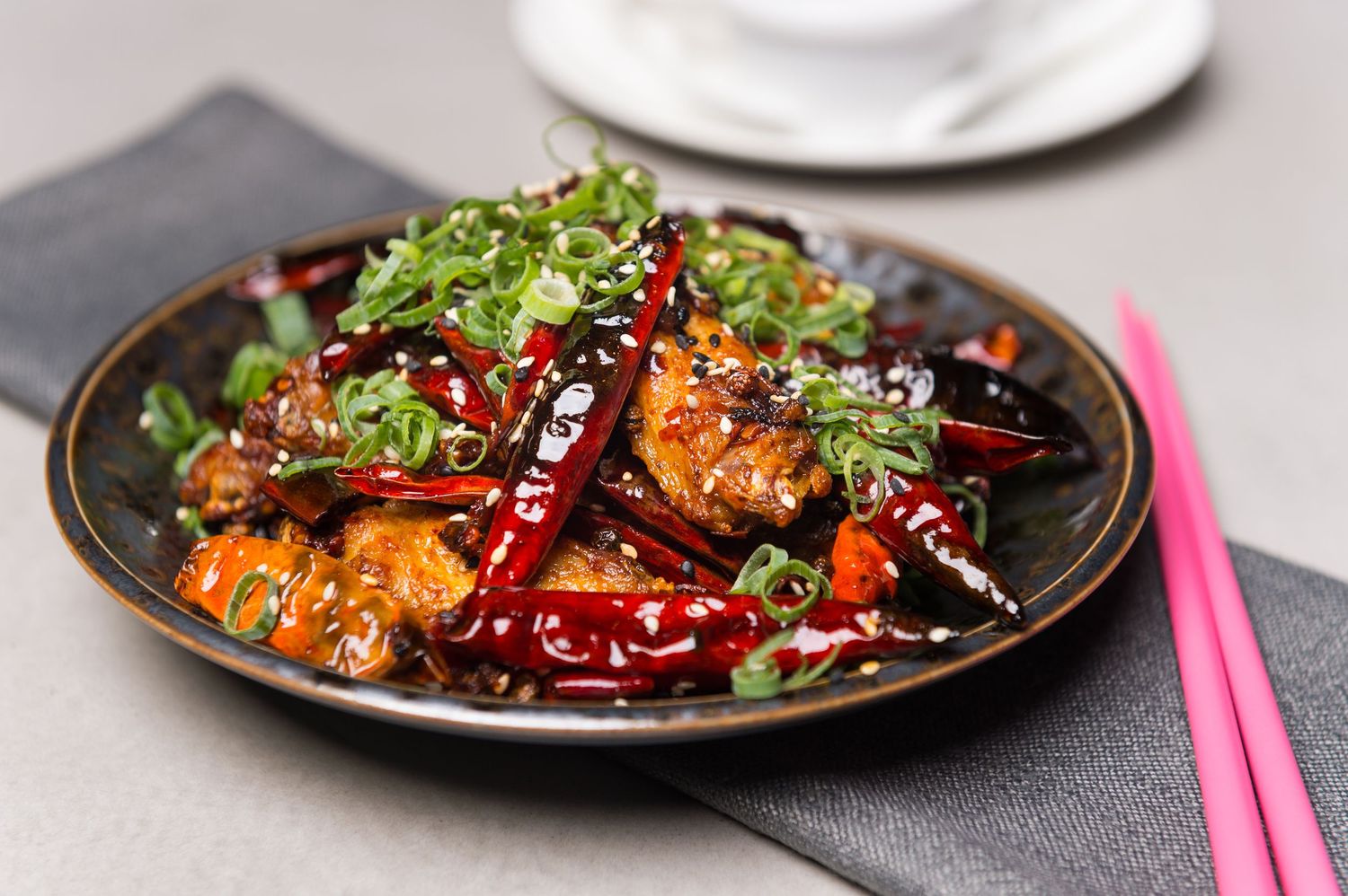 Spicy Asian stir-fry dish with red chilies and green garnish in dark bowl.