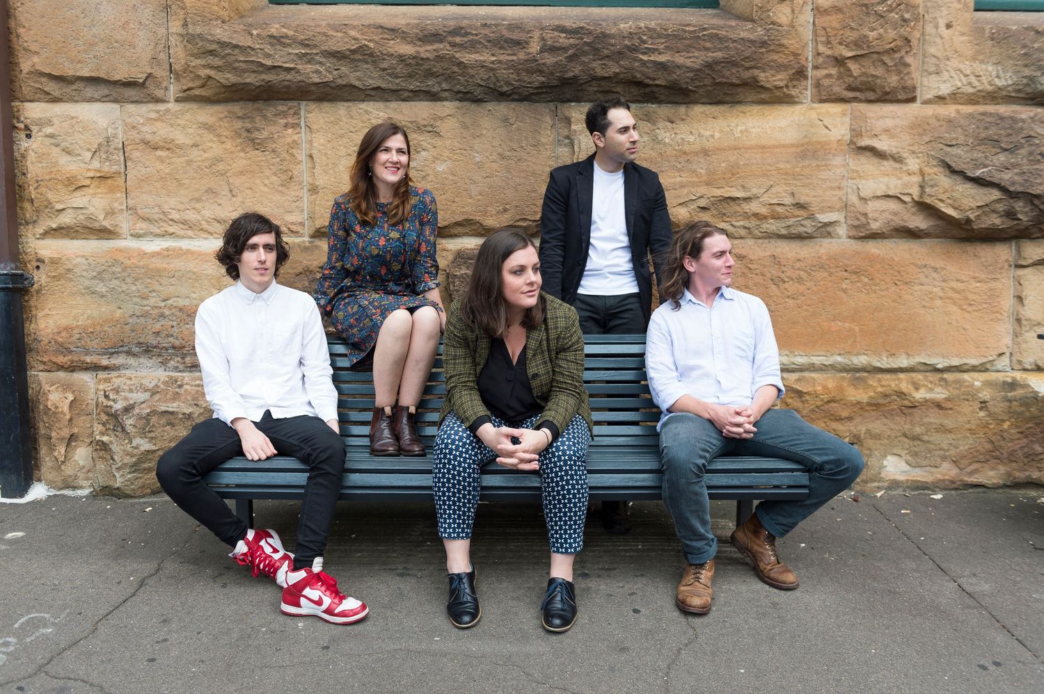 Group of young people sitting on bench against stone building exterior.