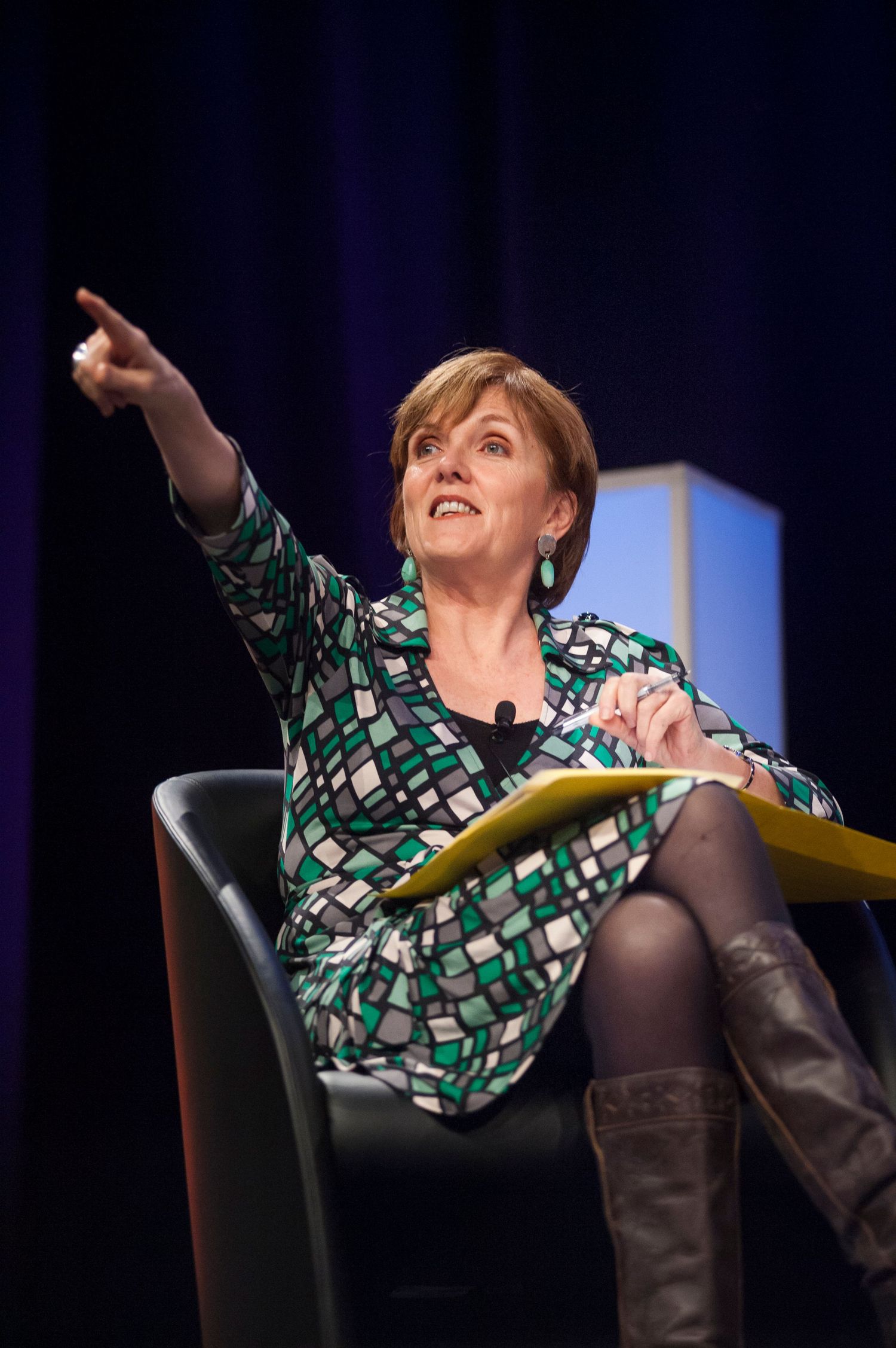 Speaker Jenny Brockie in geometric print dress gesturing animatedly during stage presentation at Sydney International Convention Centre.