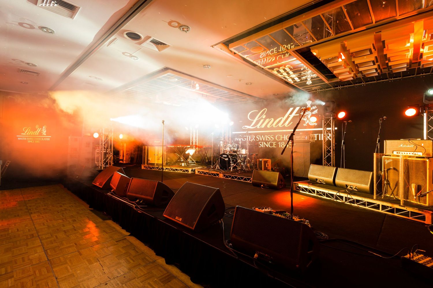 Empty music venue stage with red lighting and sound equipment set up for a performance.