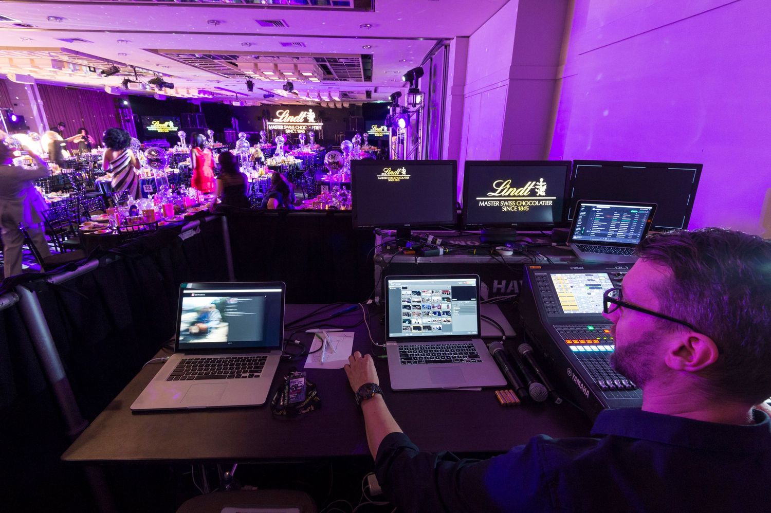 A dimly lit room with purple ambient lighting shows multiple computer workstations and monitors arranged in rows.