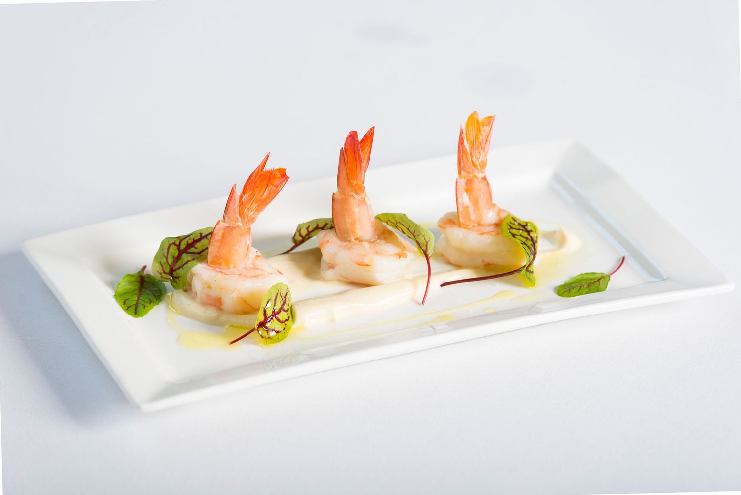 Elegant plating of shrimp appetizers on white rectangular plates with herb garnish.