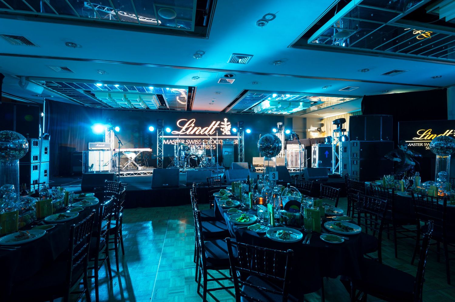 A dimly lit nightclub interior bathed in blue lighting shows empty tables and dance floors with modern decor and ambiance.