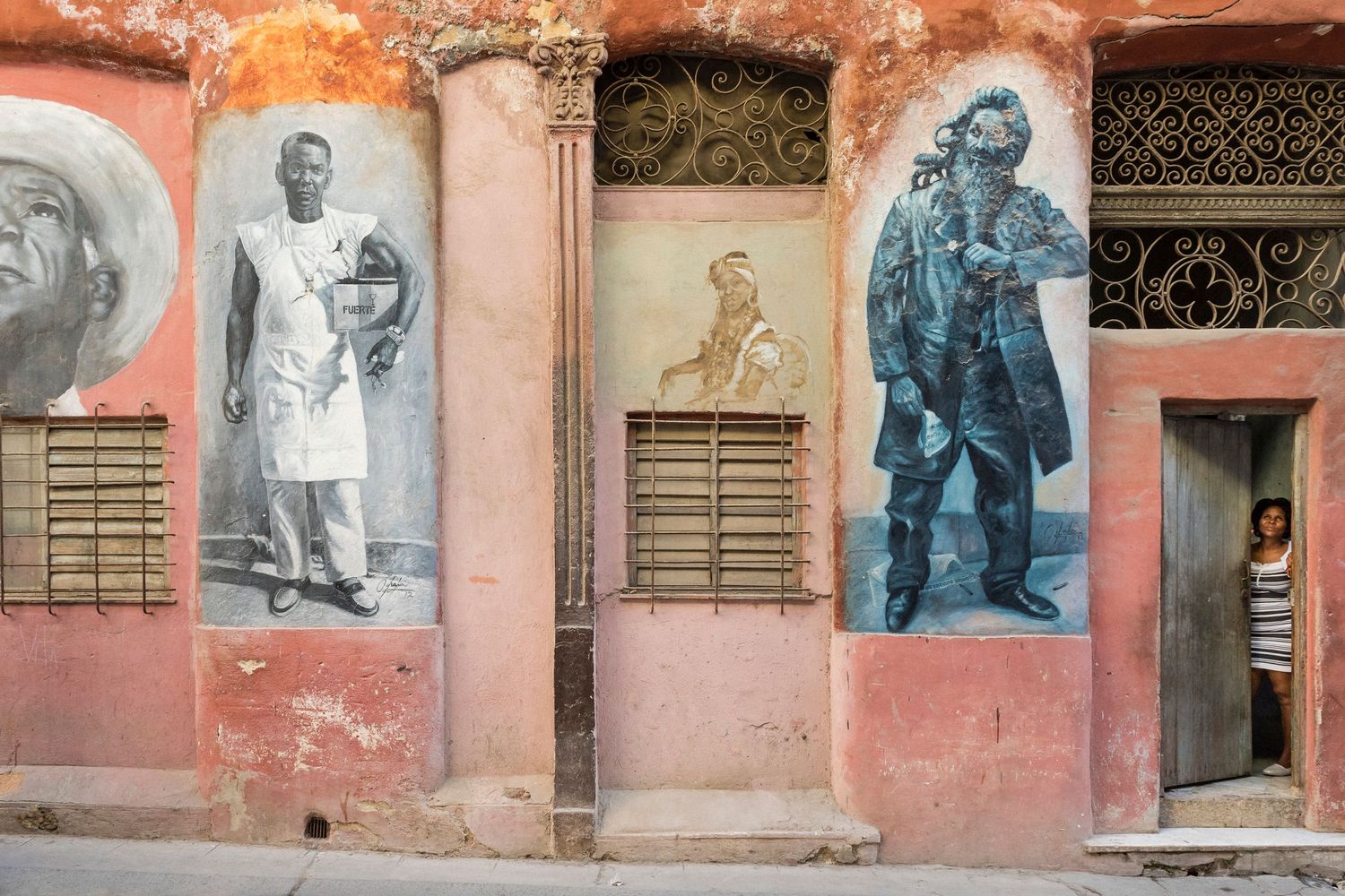 Vintage photographs displayed on weathered pink wall showing historical scenes.