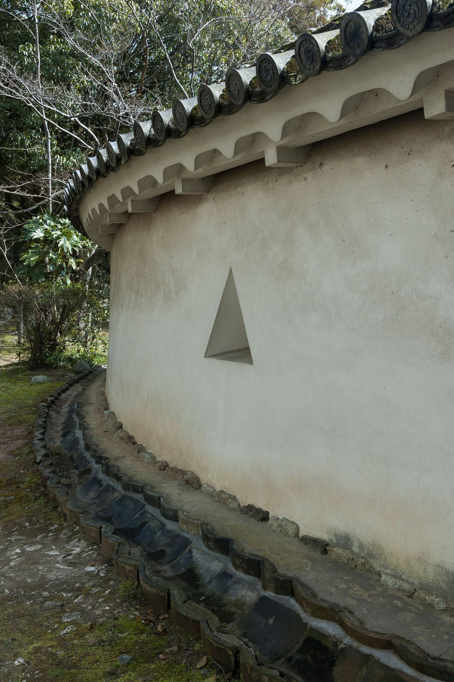 Curved white temple wall with traditional tile roof and garden path.