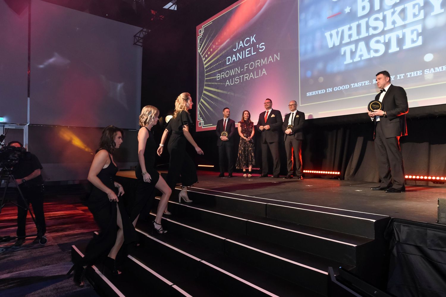People walking on a dark stage with red and blue lighting during an awards event presentation.
