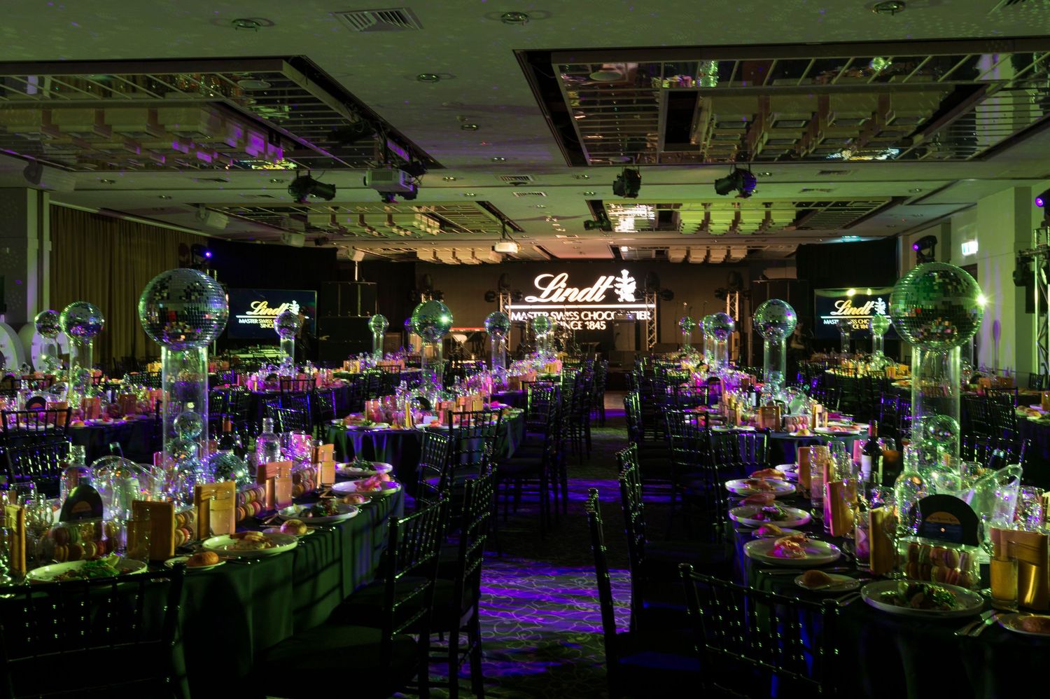 Panoramic view of an elegant wedding reception venue with purple uplighting and crystal chandeliers.