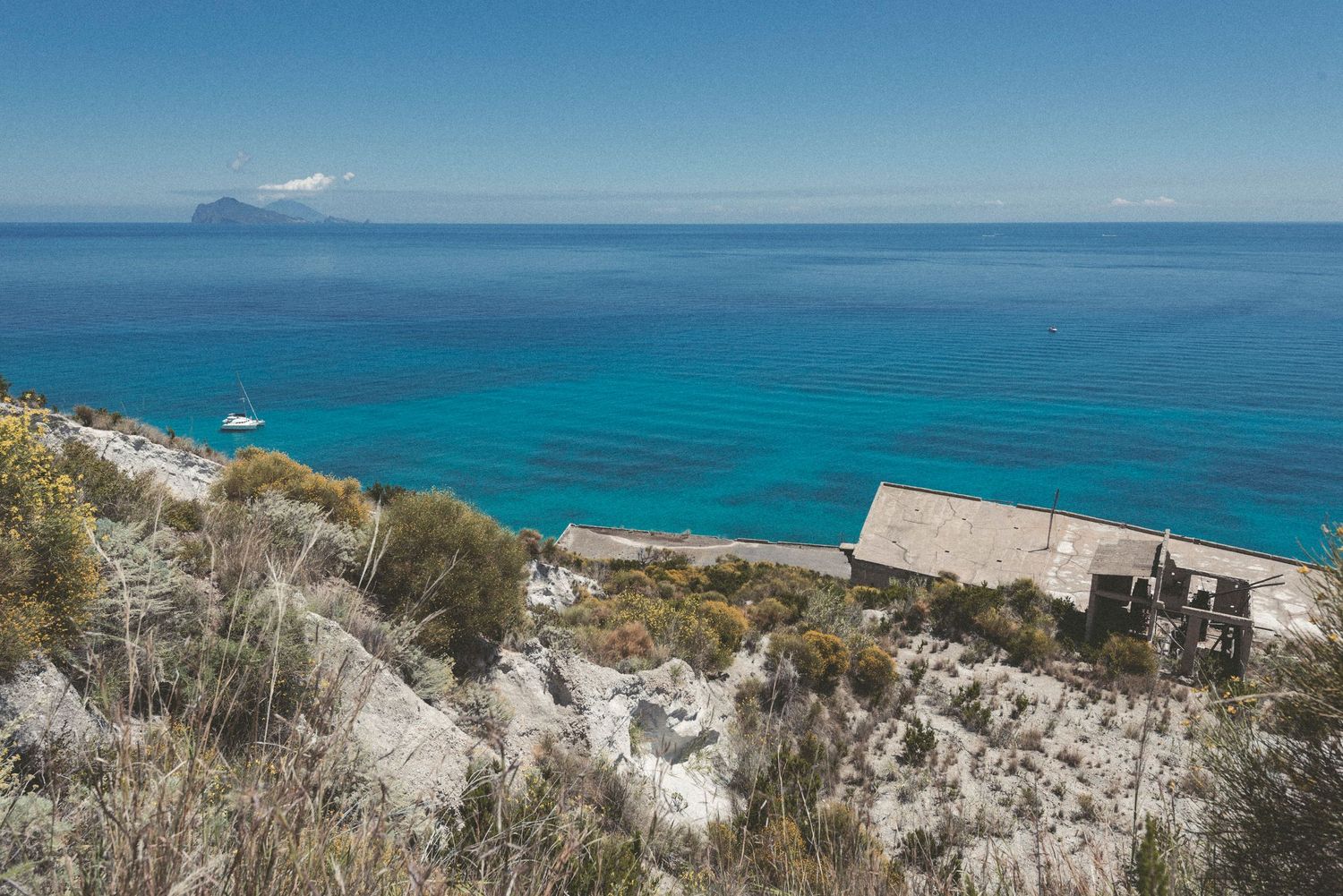 Panoramic view of turquoise Mediterranean waters and rocky coastal cliffs stretching along a sunny shoreline.