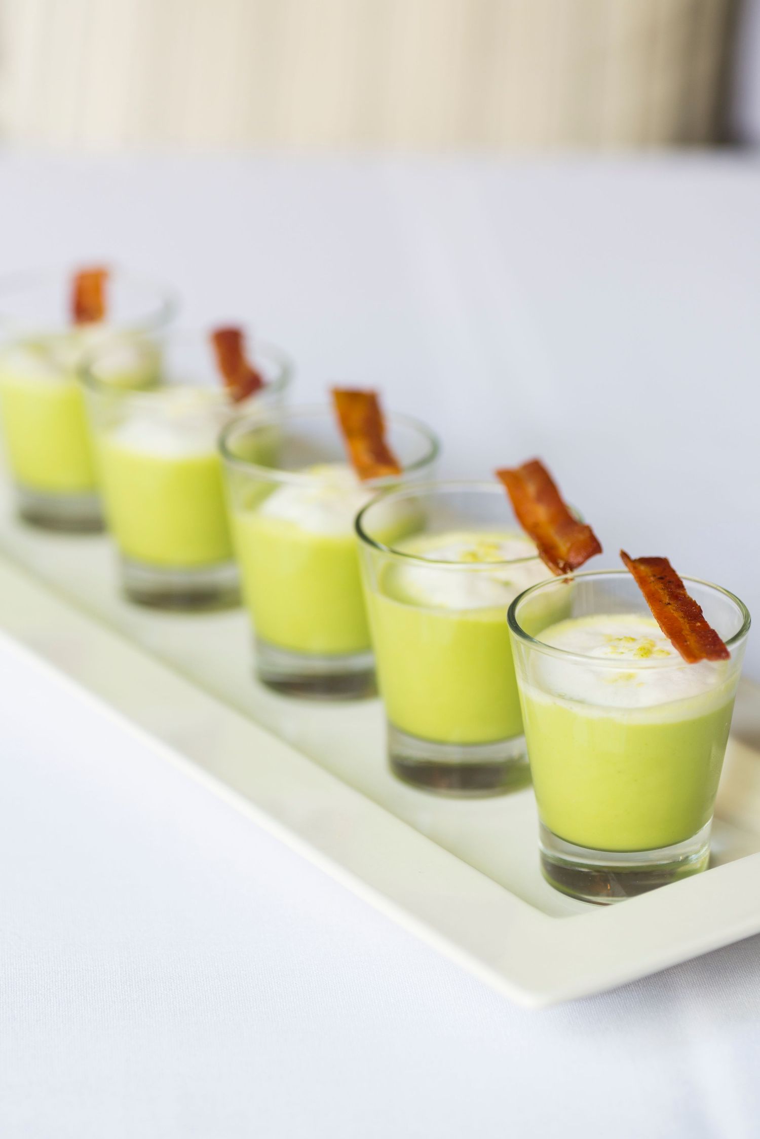 Row of lime green dessert shots topped with crispy bacon garnish.