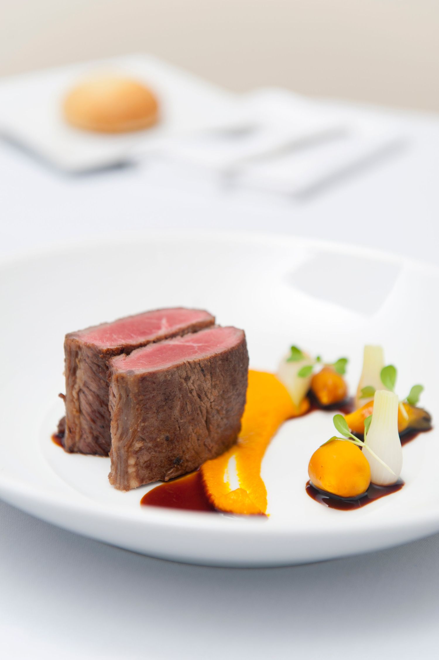 Perfectly cooked beef medallions plated with orange segments and sauce on white dinnerware.