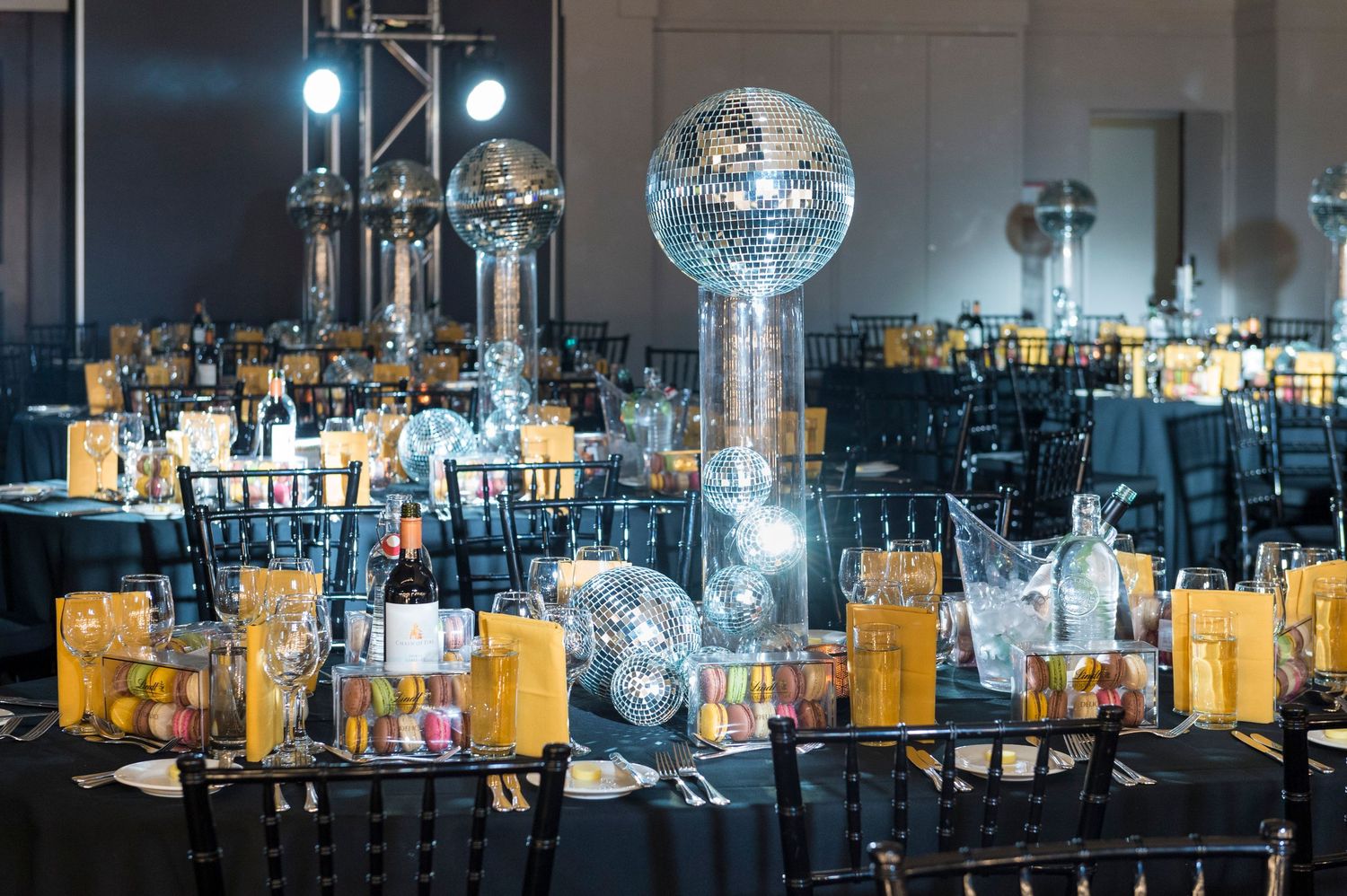 Elegant banquet hall setup with glowing centerpieces, glass decorations, and black chairs at round tables.