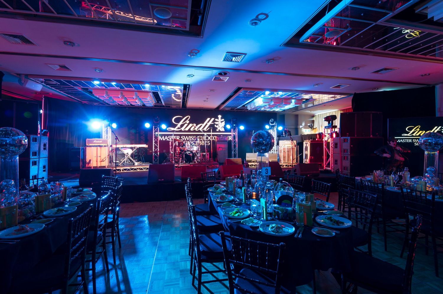 Elegant event venue with blue and red mood lighting illuminating dining tables and chairs in a dark banquet hall.