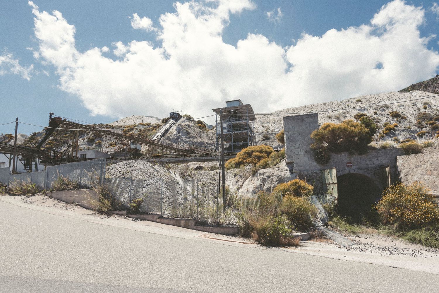 Panoramic view of a white limestone quarry with industrial equipment and buildings against a bright blue sky.