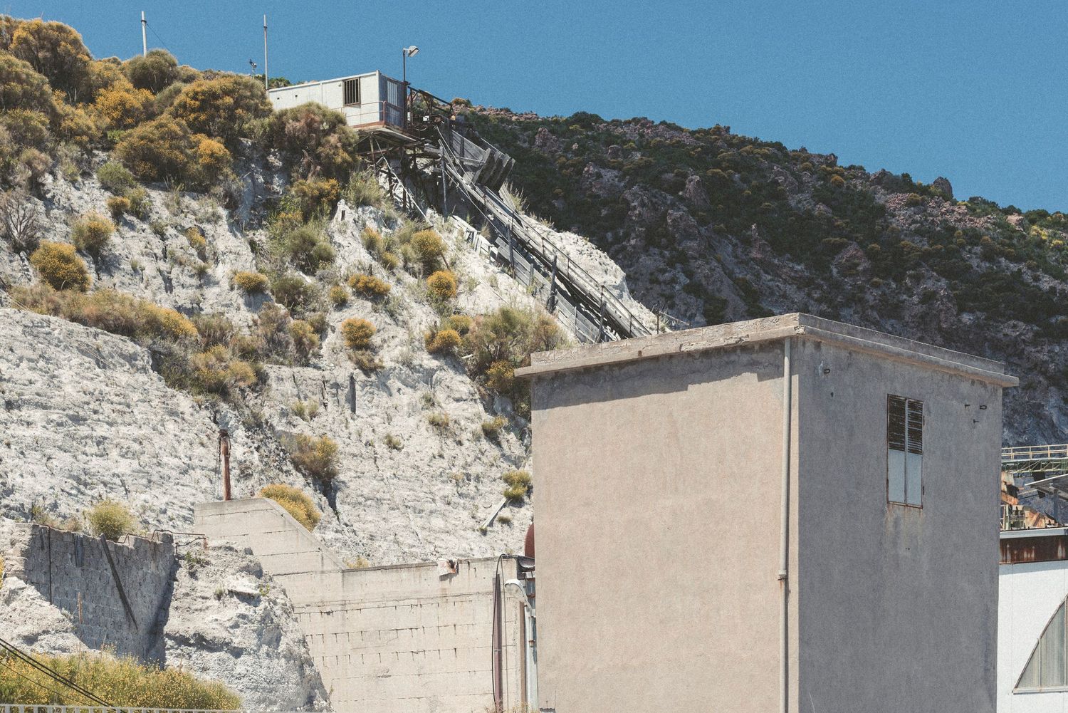 Panoramic view of white buildings nestled against a rocky hillside under bright blue sky.