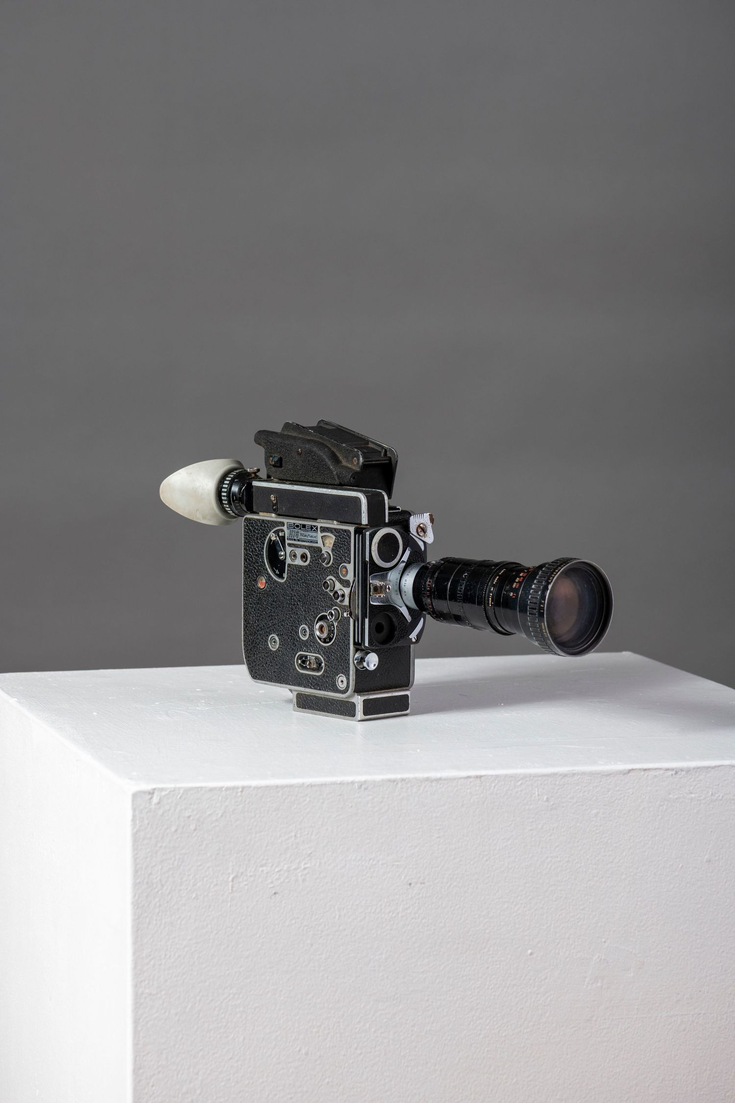 A vintage black film camera with telephoto lens displayed on a white surface against a gray background.