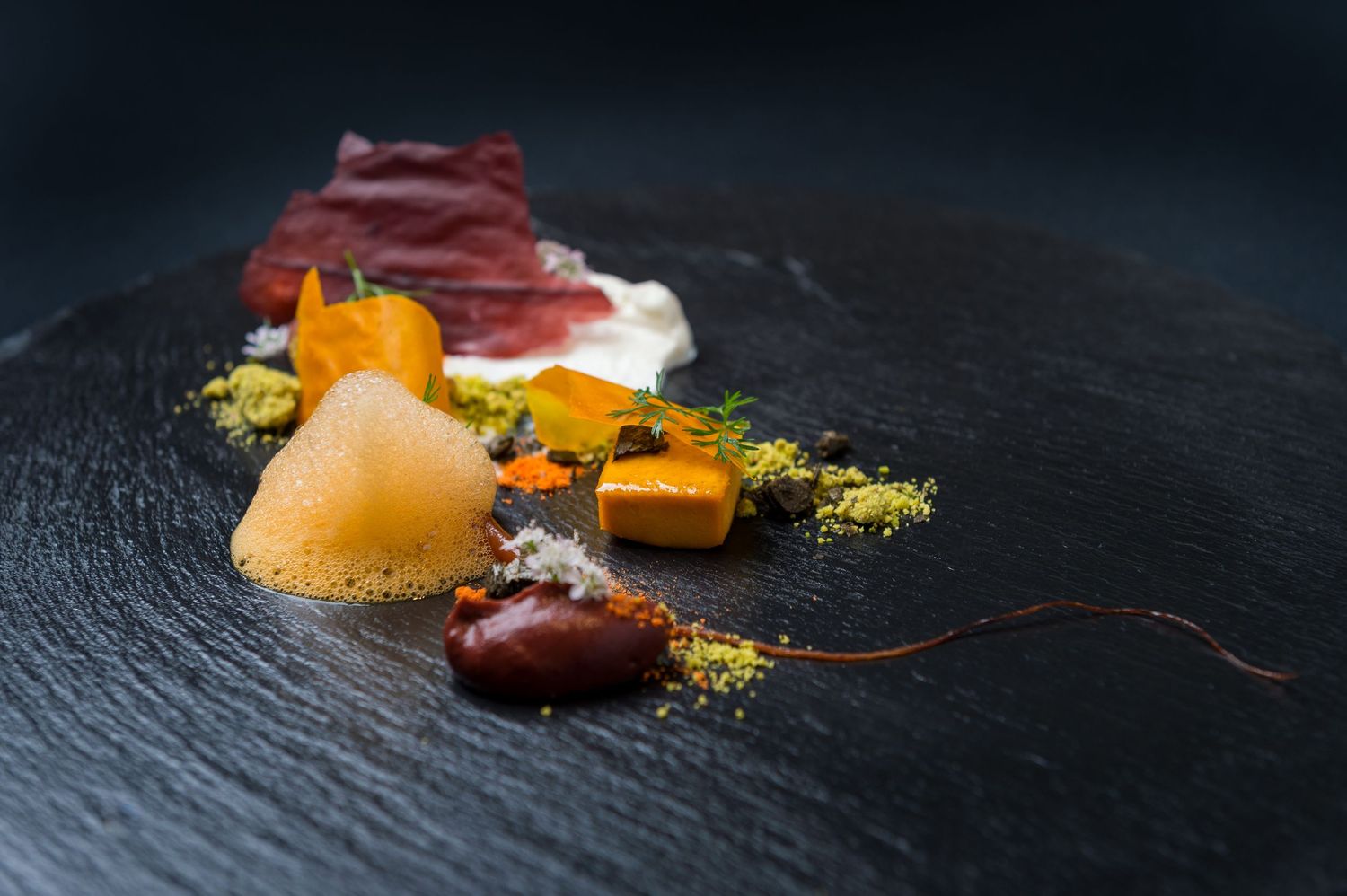 Artistic plating of seafood and sauces on dark slate with vibrant yellow accents.