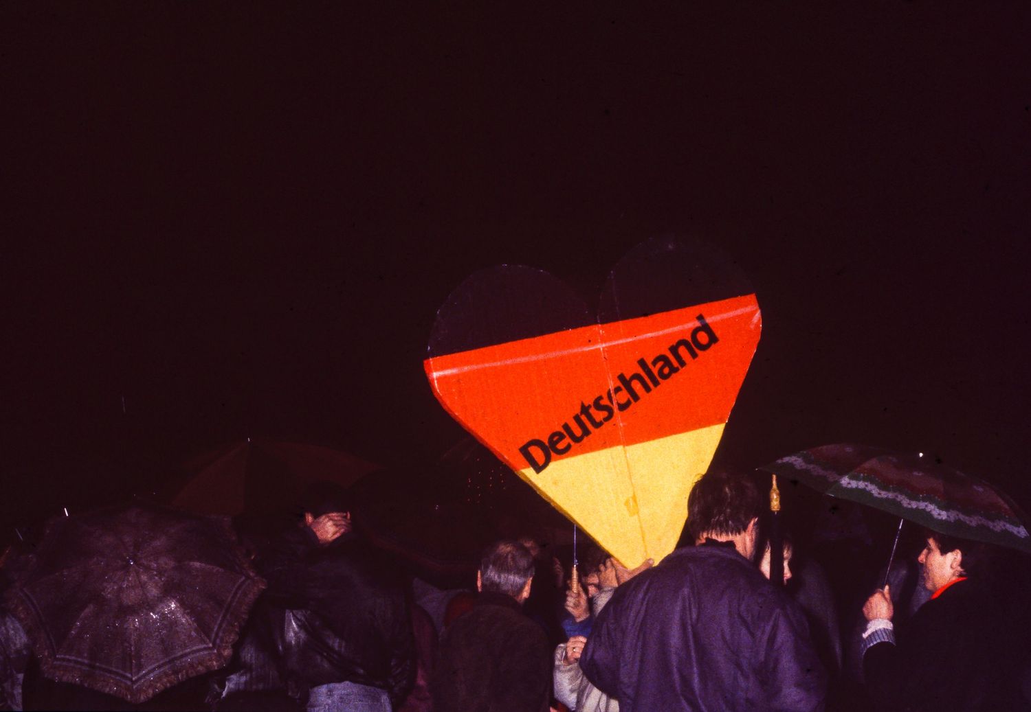 Orange and yellow triangular signs glowing in the darkness at a nighttime gathering.