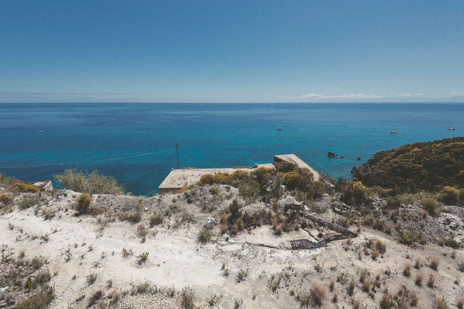 Panoramic view of white sandy dunes against a vibrant blue ocean and sky along a pristine coastline.