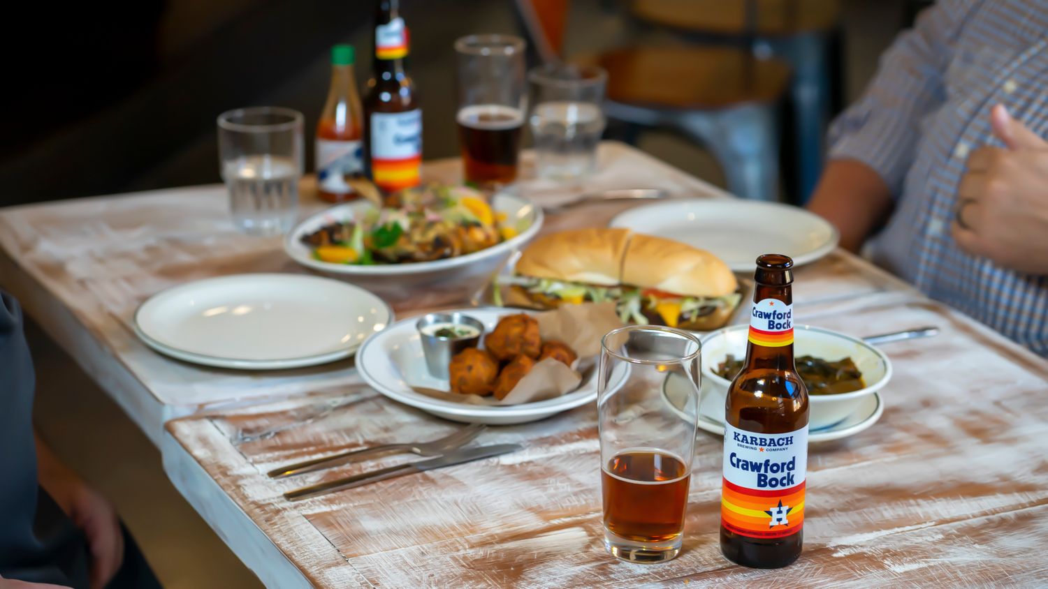 Crawford Bock beer bottle on rustic white wood table with burger and food dishes.