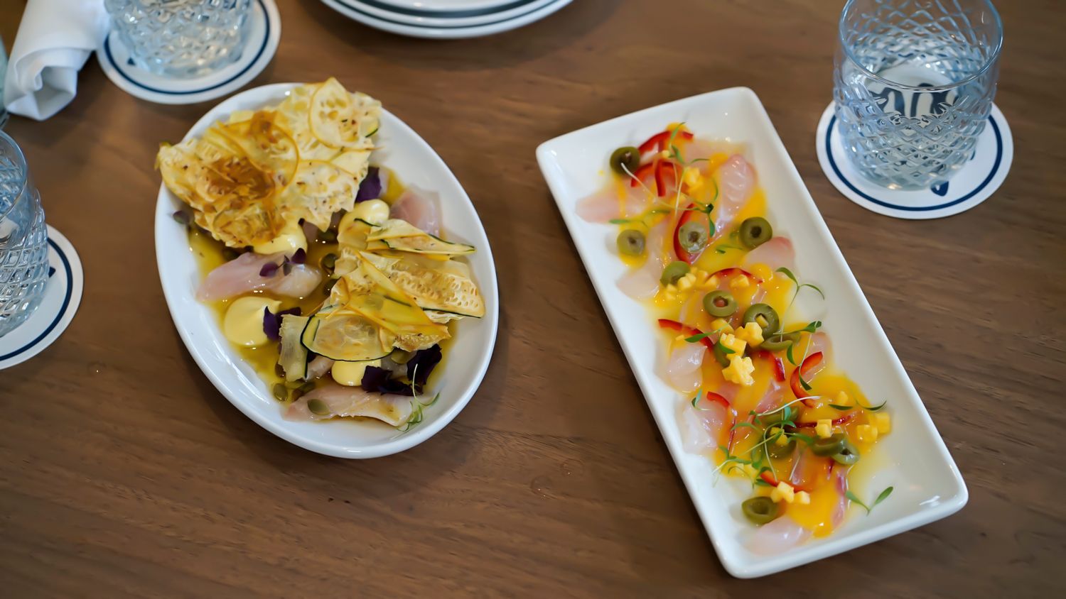 Two appetizer plates featuring crackers with toppings and a colorful pepper and citrus salad on a wooden table.