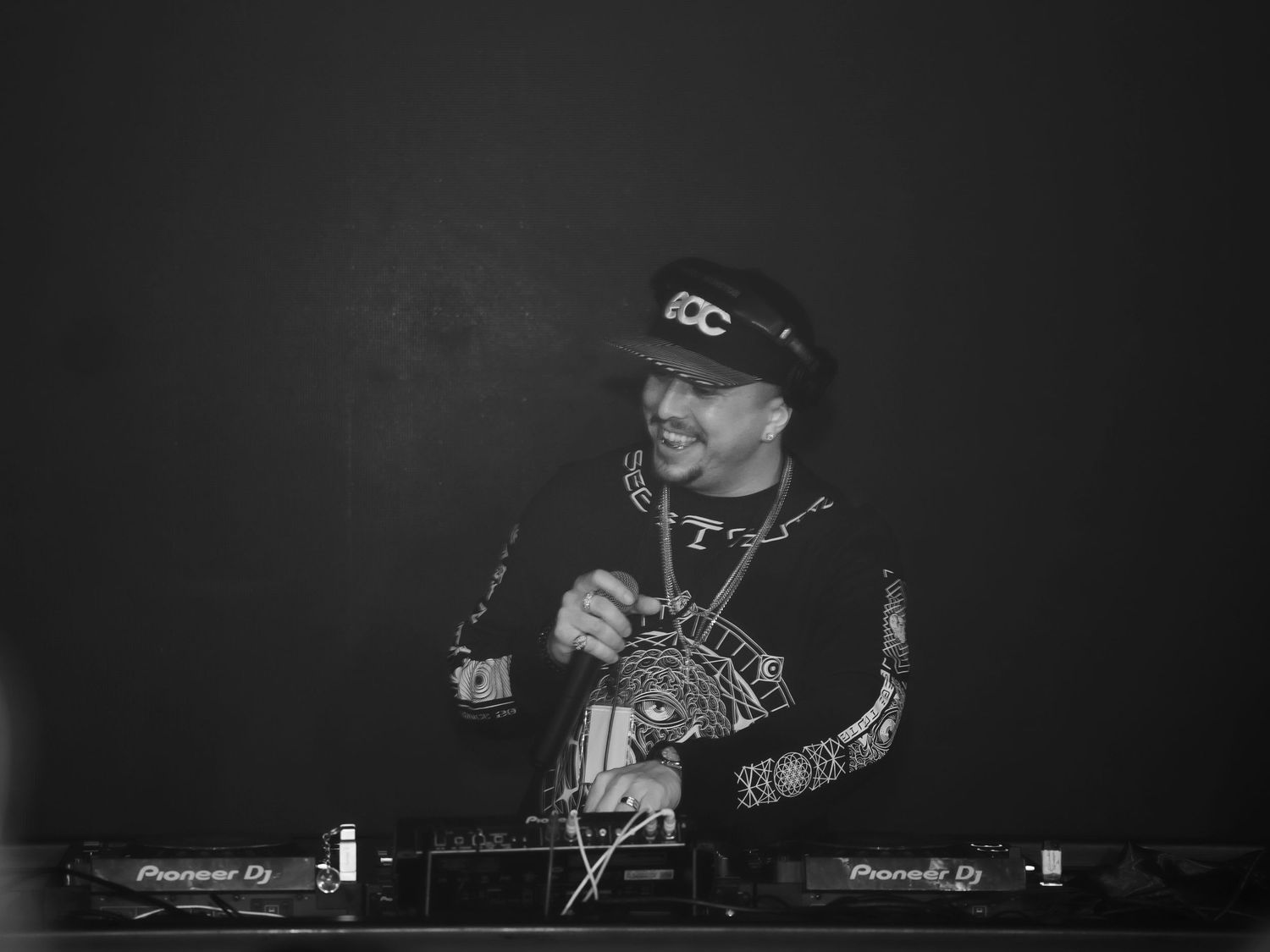 Black and white photo of a smiling DJ performing behind Pioneer DJ turntables.