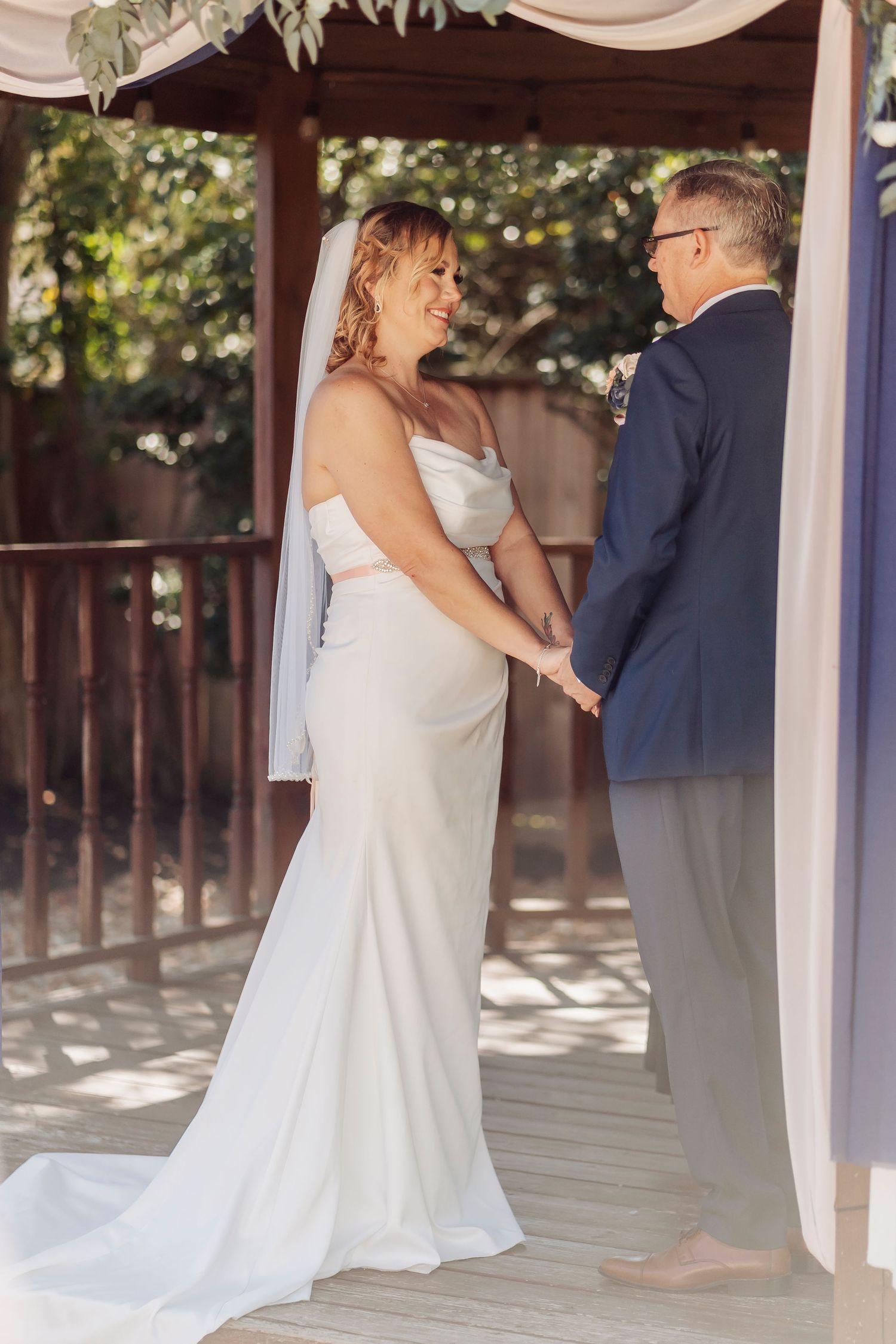 Bride and groom hold hands at outdoor wedding ceremony, bride wearing elegant white gown with veil.