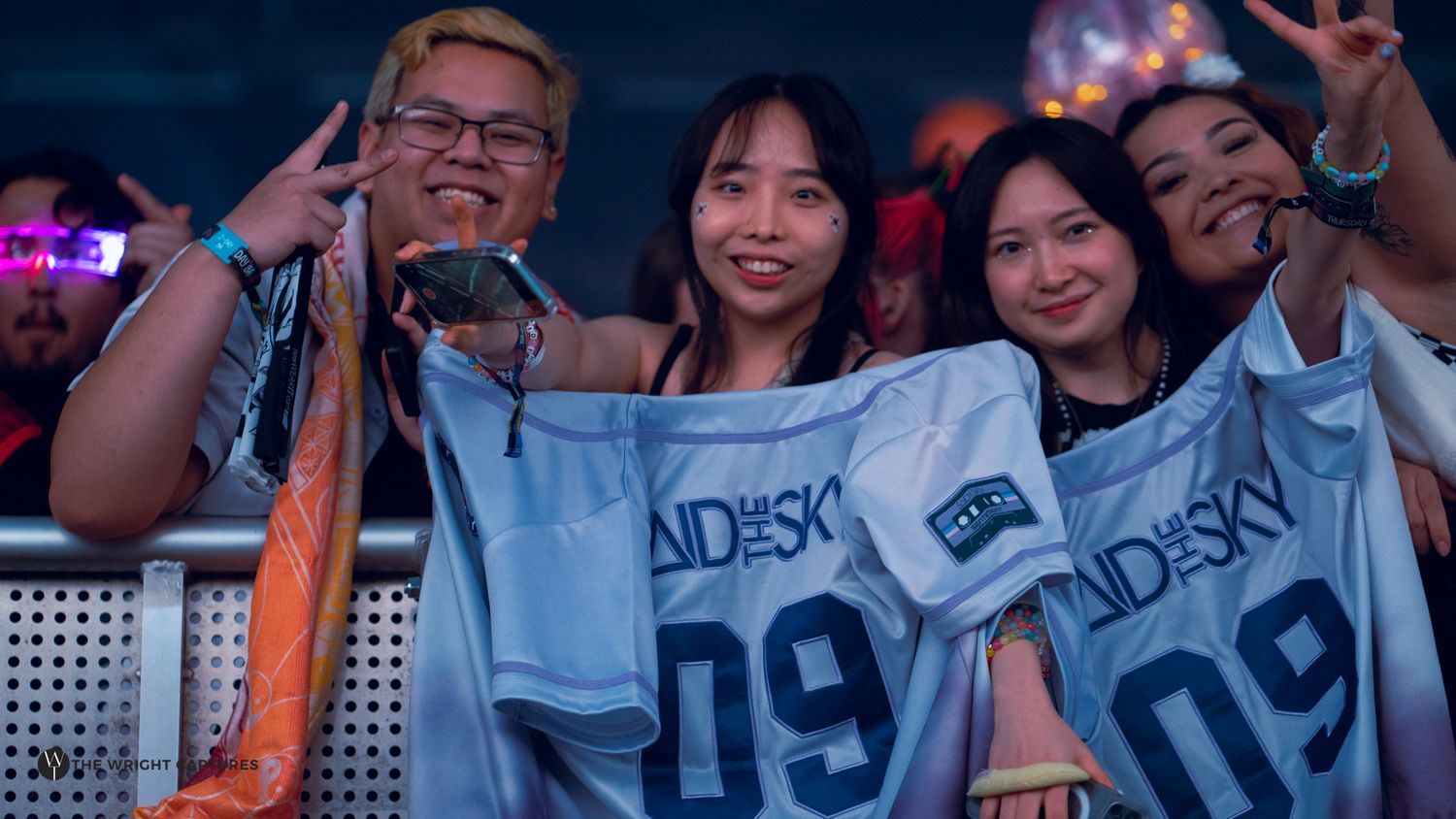 Excited fans holding Andesky jerseys at a vibrant concert event, posing with peace signs and smiles.