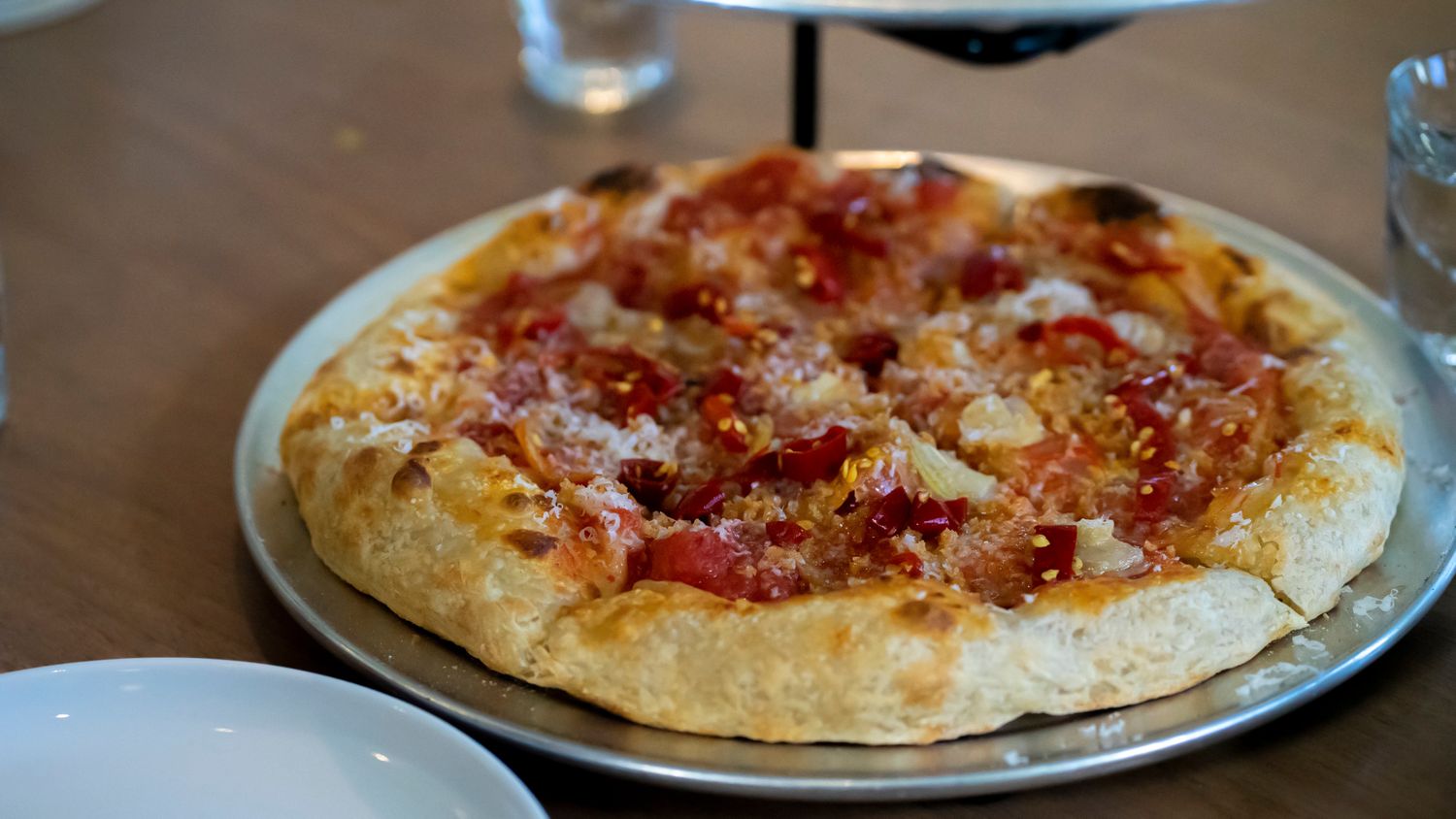 A golden-crusted pizza topped with tomato sauce, cheese, and meat on a silver tray at a restaurant.