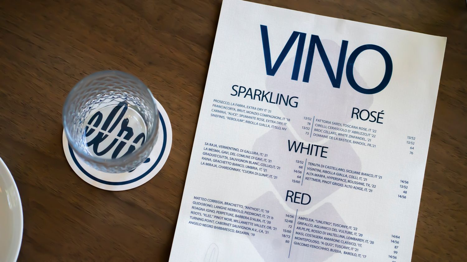 A VINO wine menu listing sparkling, rosé, white, and red wines beside a branded coaster on a wooden table.