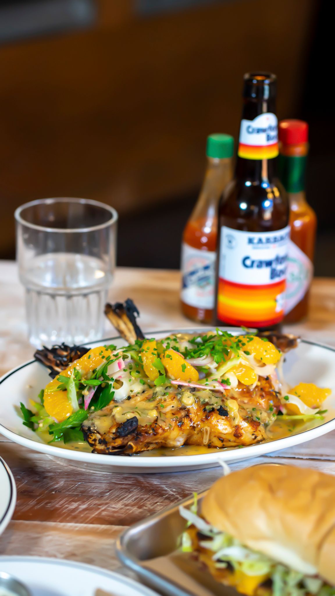 Grilled fish dish with citrus garnish and herbs served with Crawford Bock hot sauce bottles.