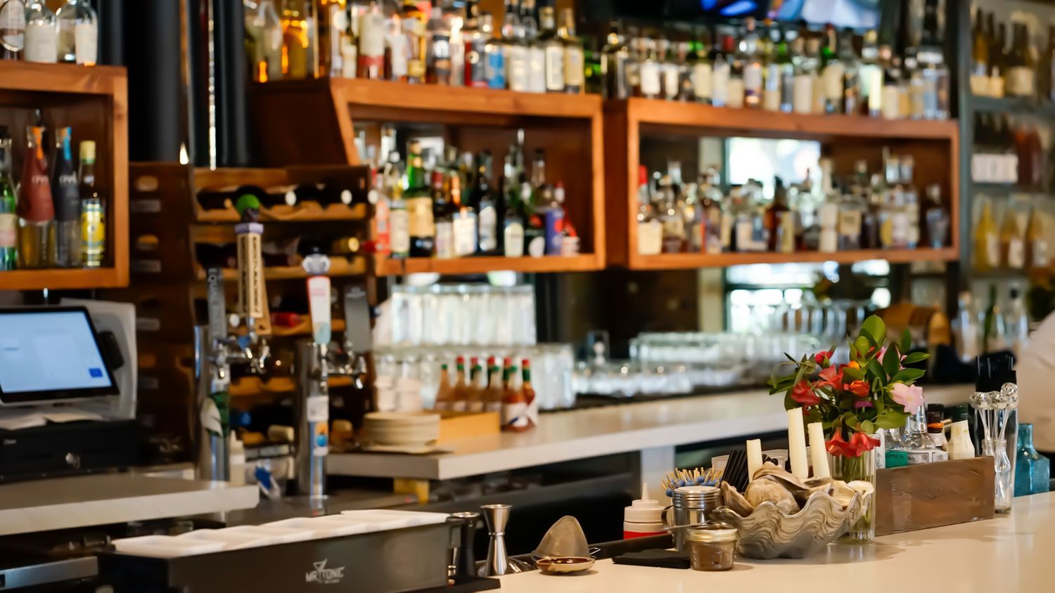 Well-stocked bar interior with wooden shelves lined with liquor bottles, beer taps, and glassware in a modern restaurant.
