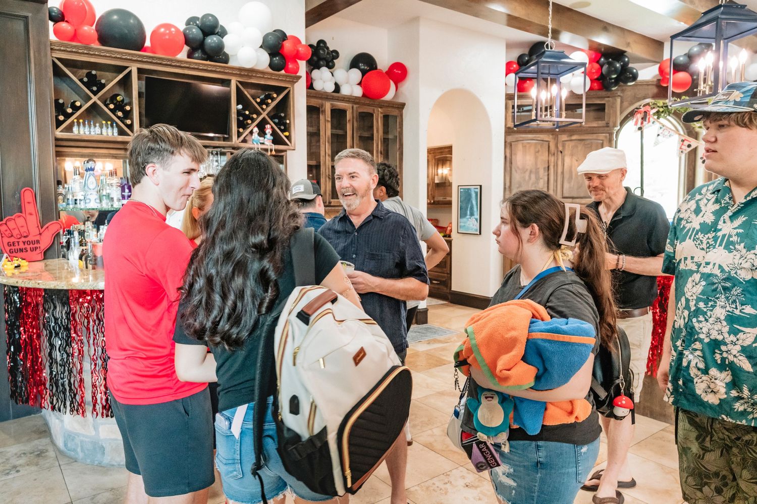 People socializing at a festive party with red and black balloon decorations in an elegant indoor venue.