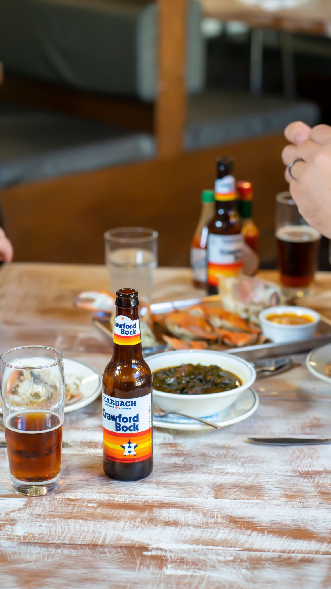 Karbach Crawford Bock beer bottle on rustic table with seafood dishes and condiments.