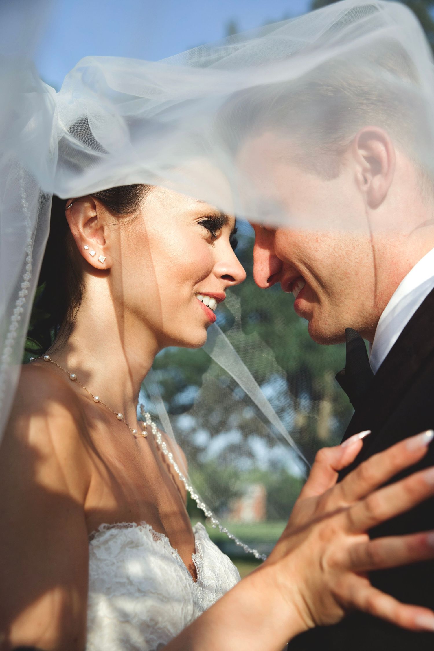 Close-up portrait of a bride and groom touching foreheads under a sheer veil, highlighting connection and emotion.