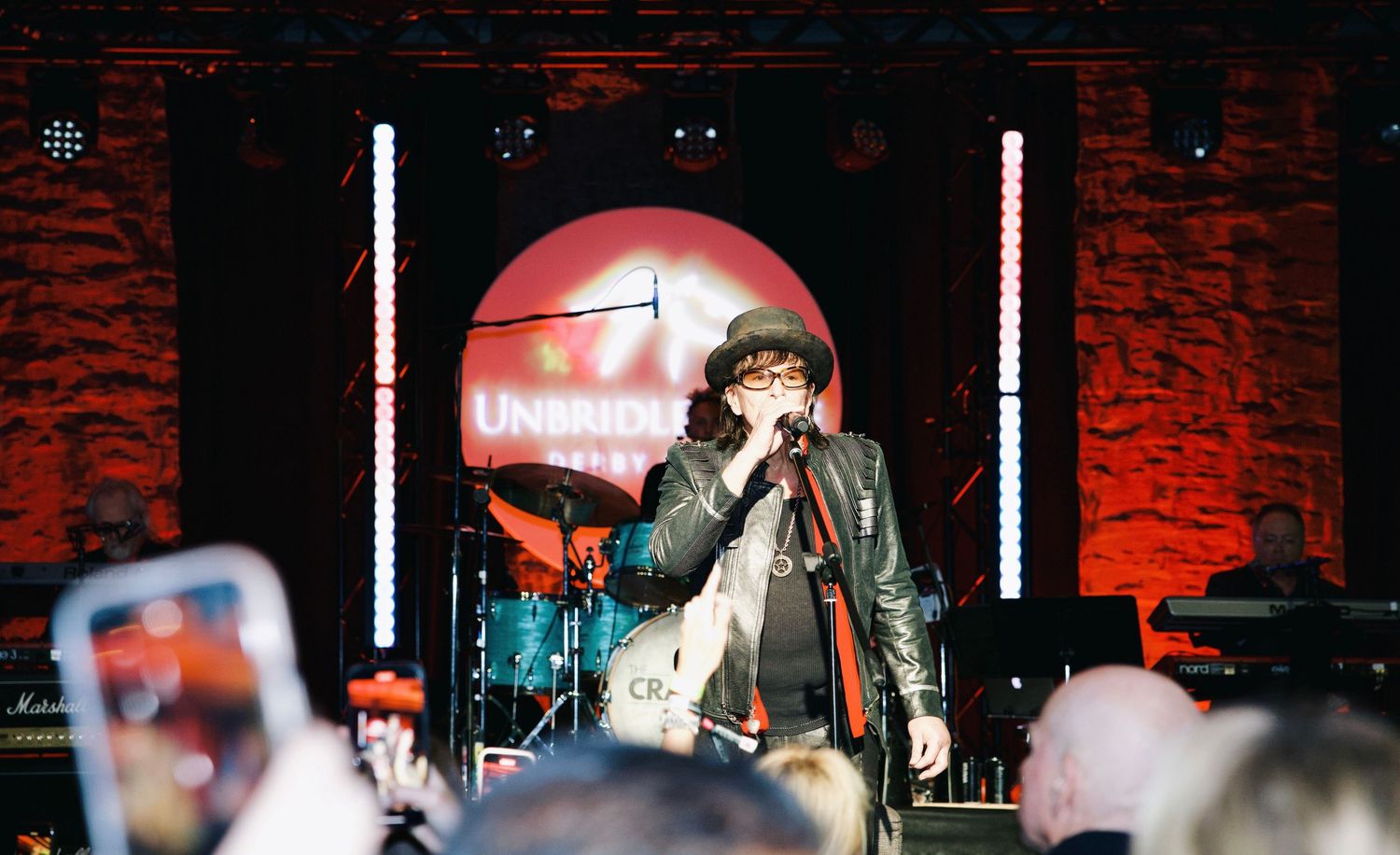 Rock vocalist sings into a microphone during a live performance, framed by colorful stage lighting and an engaged audience.
