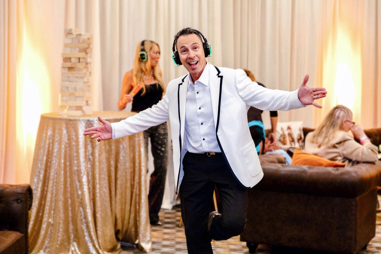 Event guest wearing headphones dances with arms open during a lively silent disco celebration in a softly lit indoor venue.