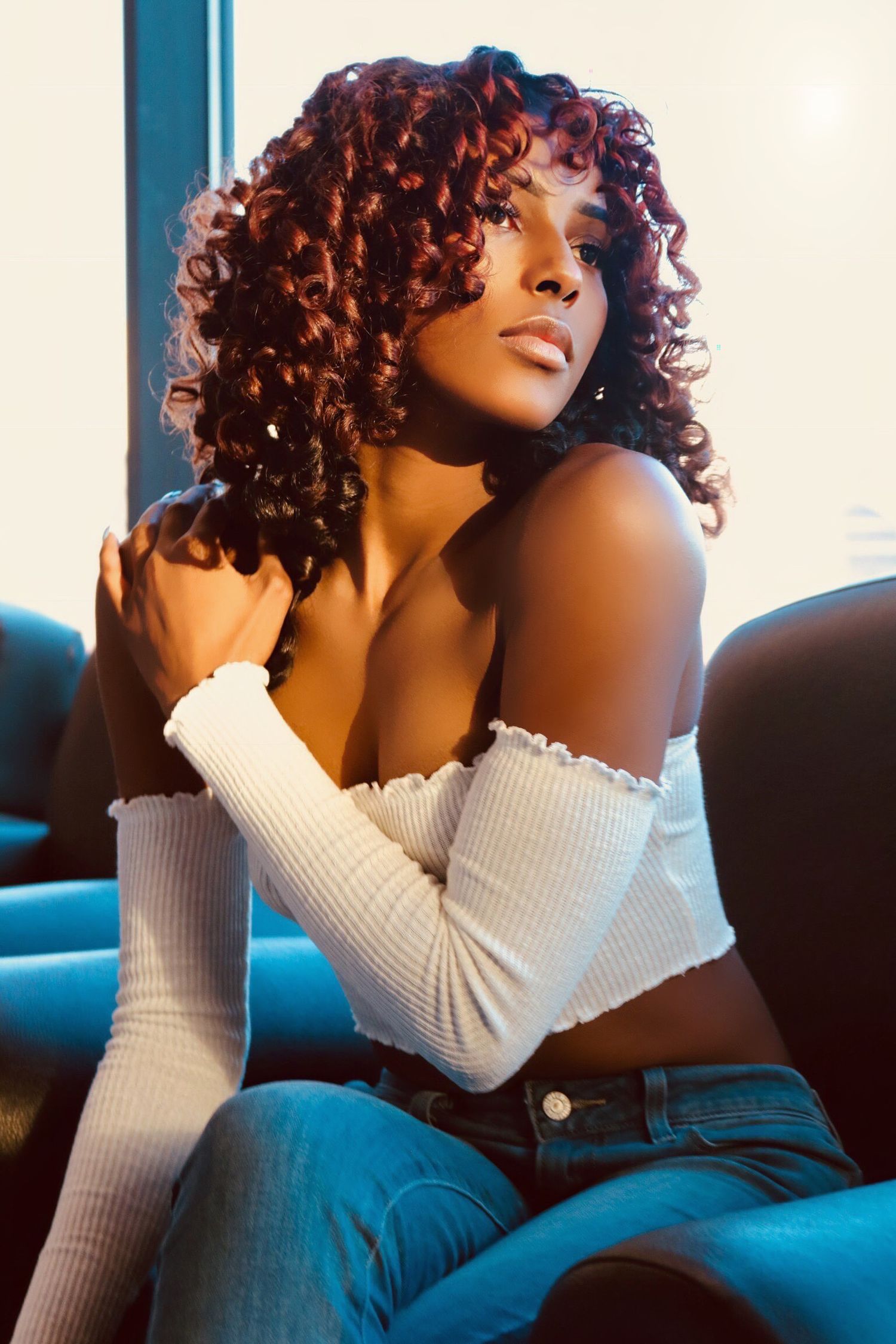 Moody indoor portrait of a woman with curly hair seated on a couch, gazing away from the camera.