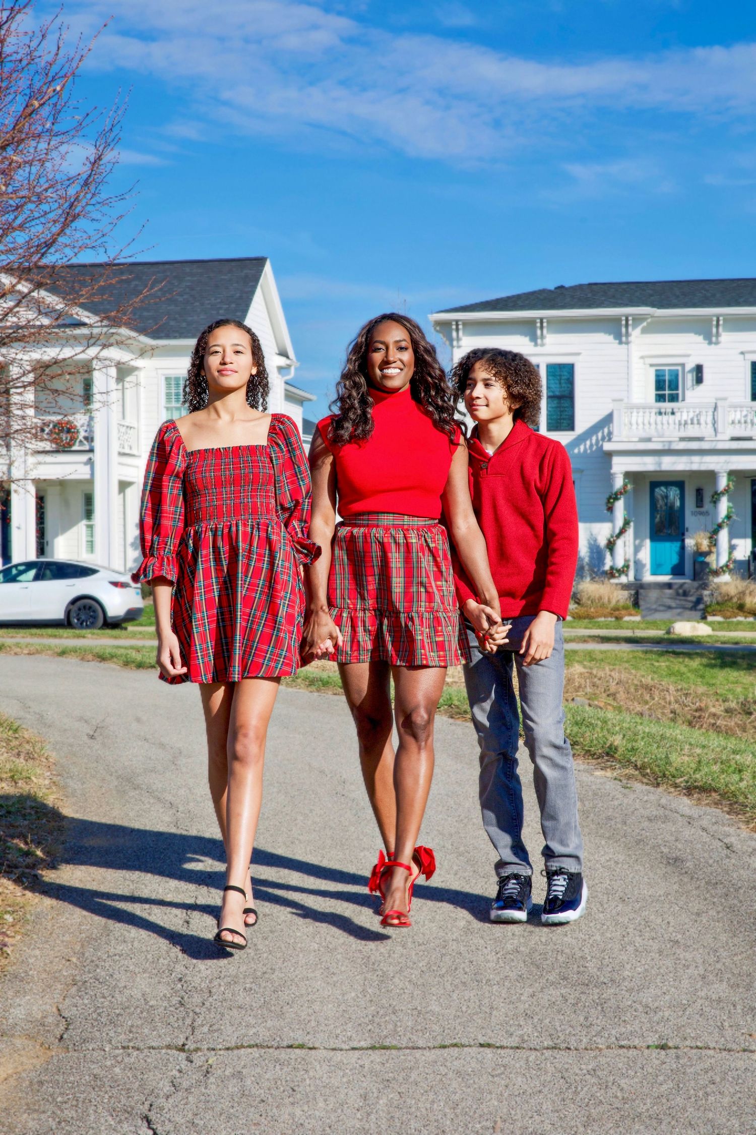 Family walking together on a sunny street, wearing red outfits against a vibrant neighborhood backdrop with bright homes and sky.