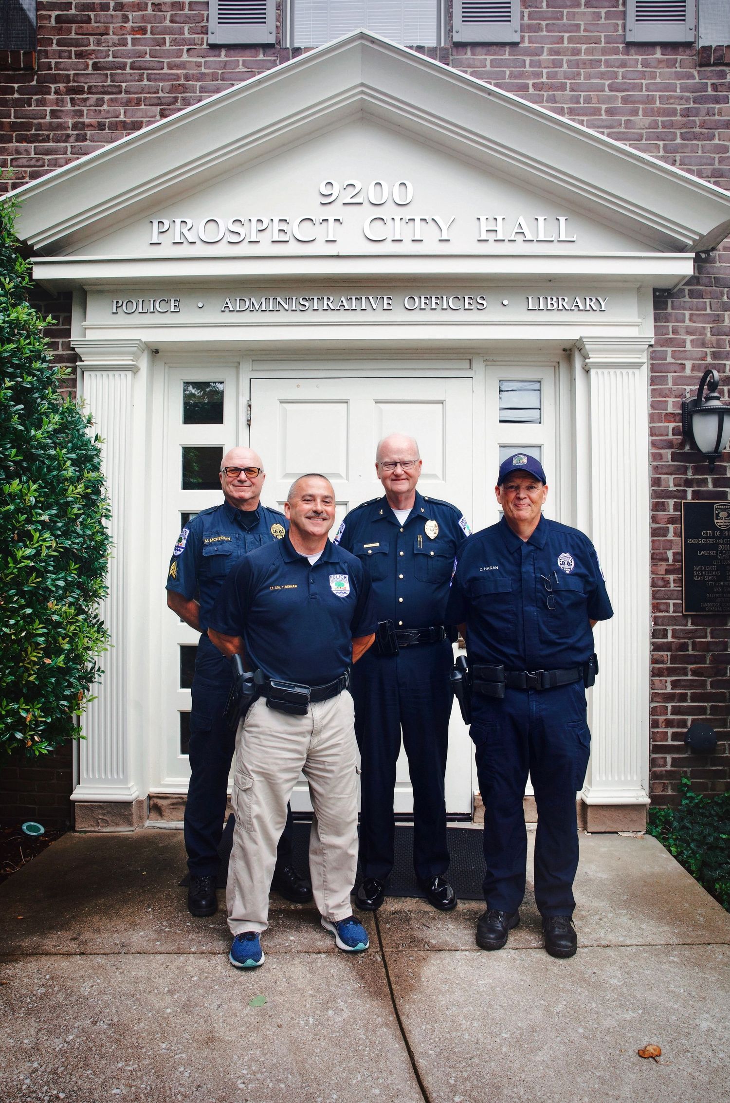 Group of uniformed police officers standing outside Prospect City Hall, posed in front of a brick building entrance.