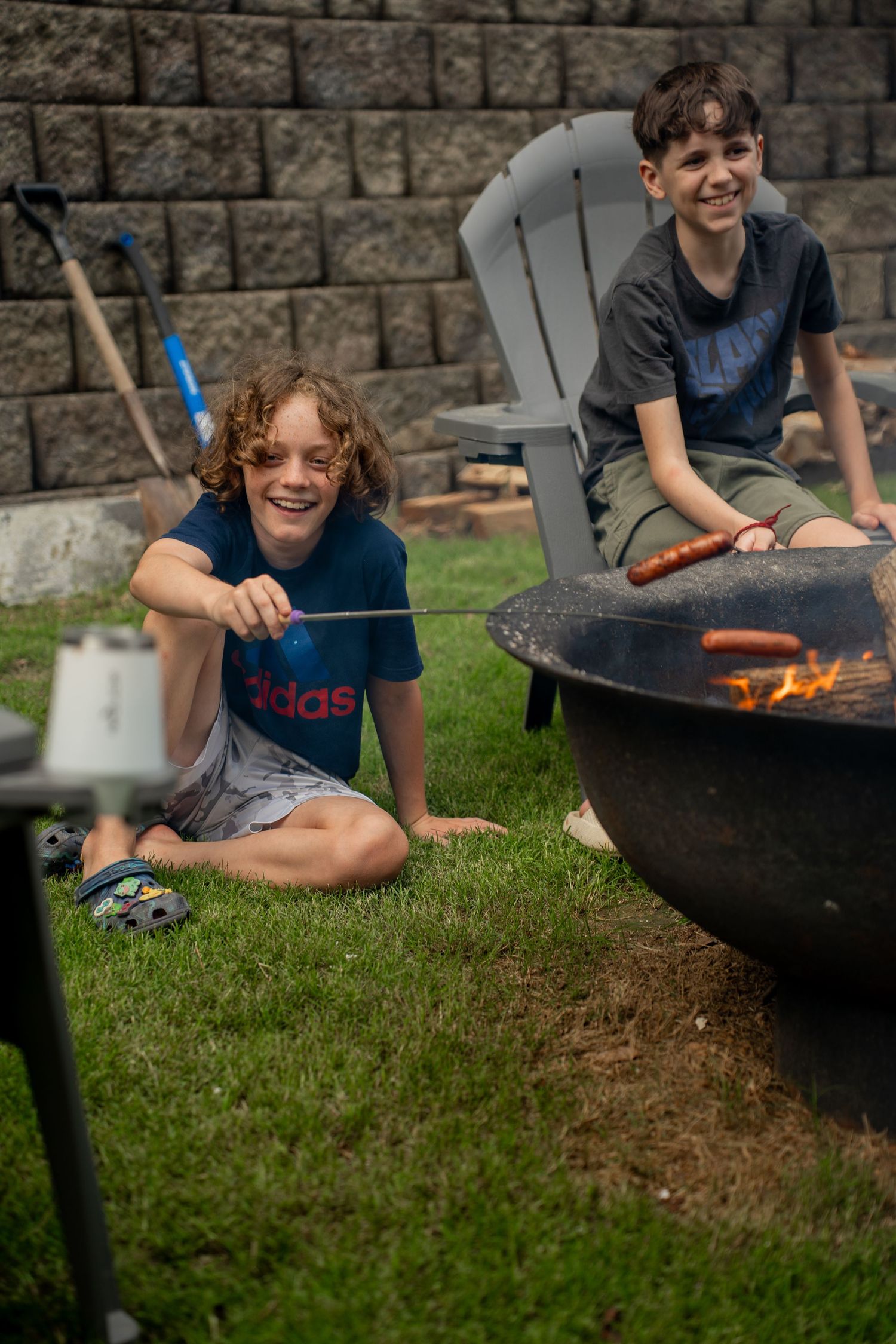 Two boys cooking hotdogs over fire outside
