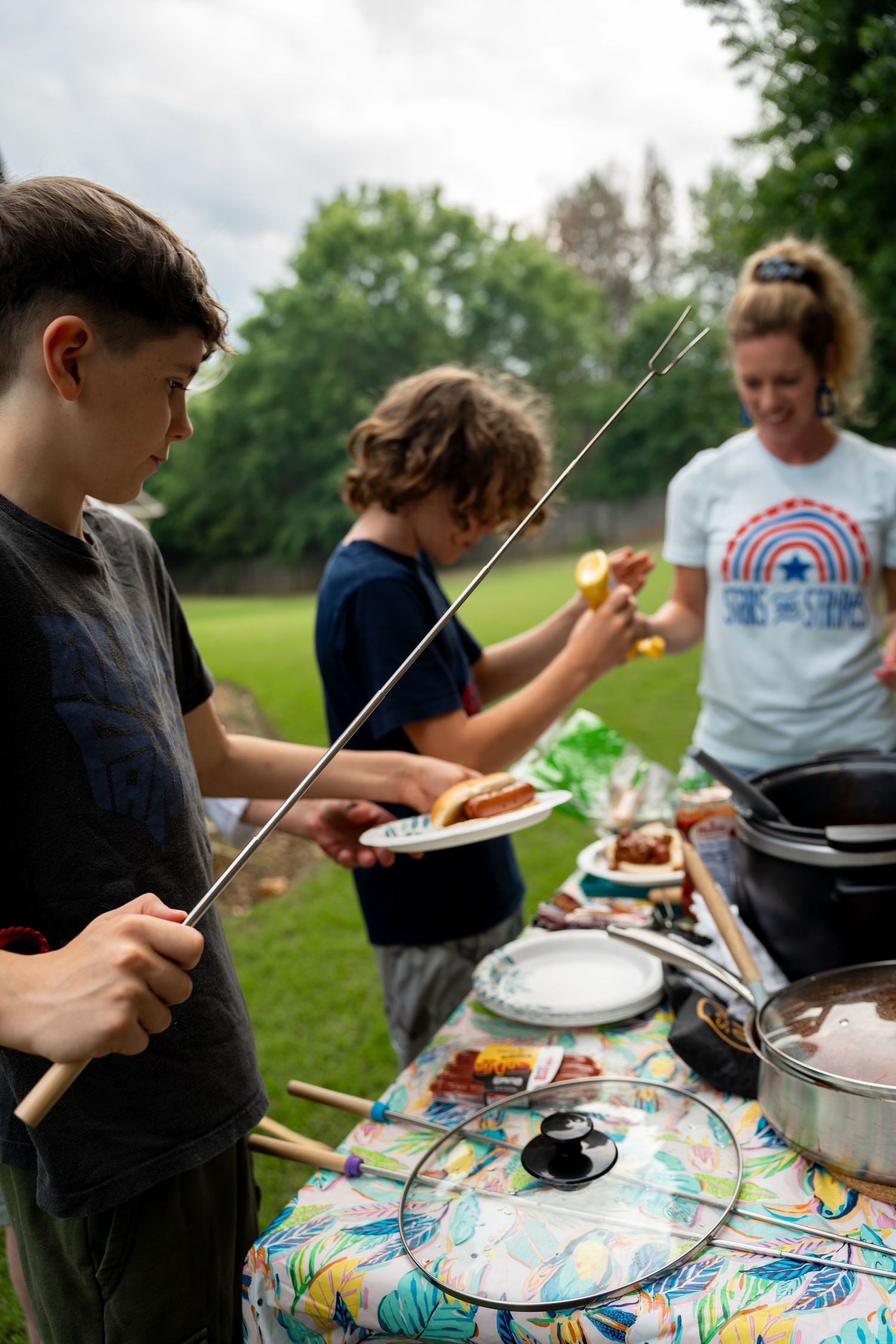 Woman and two boy serving themselves hotdogs outside