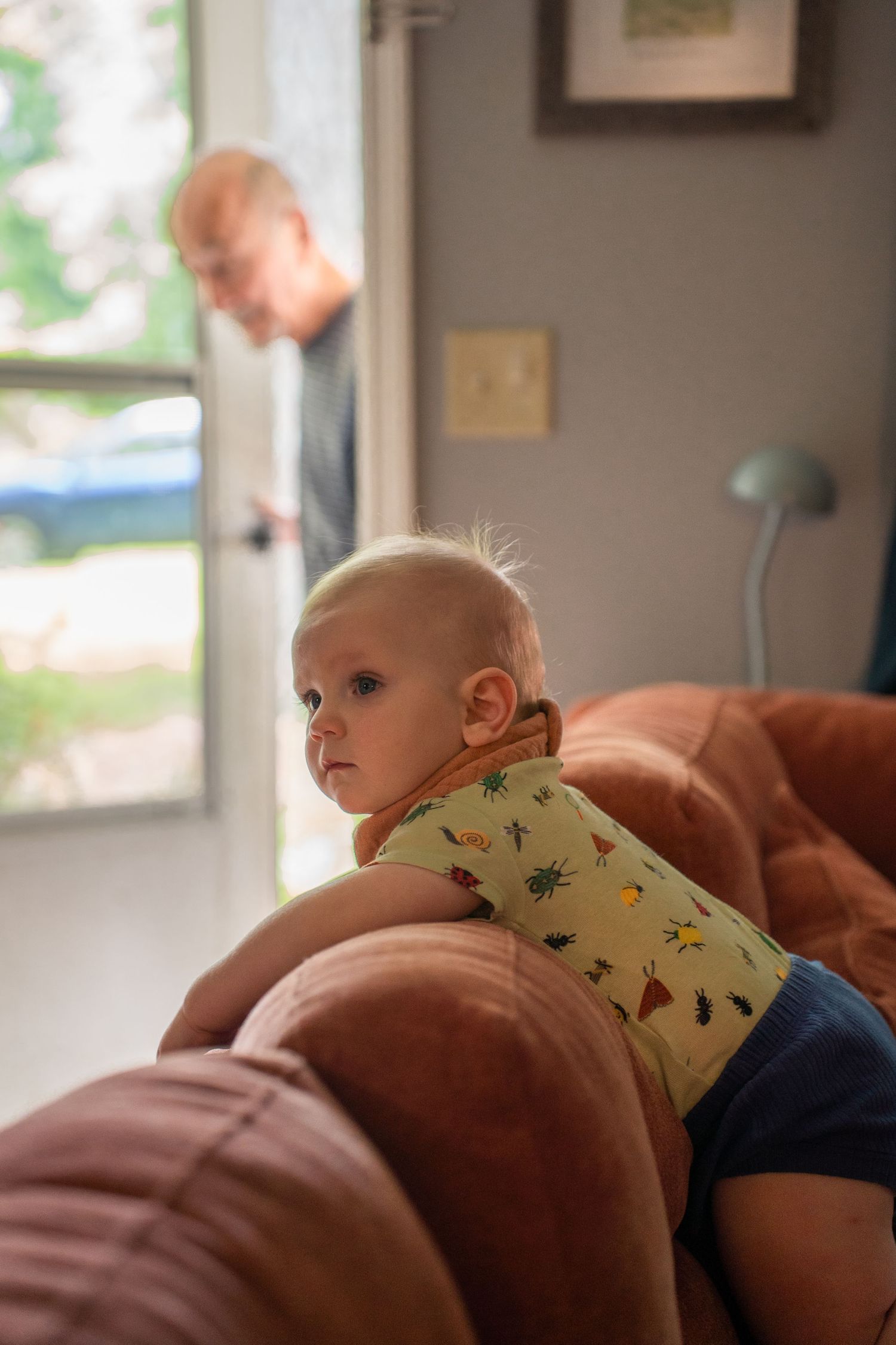 Toddler leaning over back of sofa while man enters door