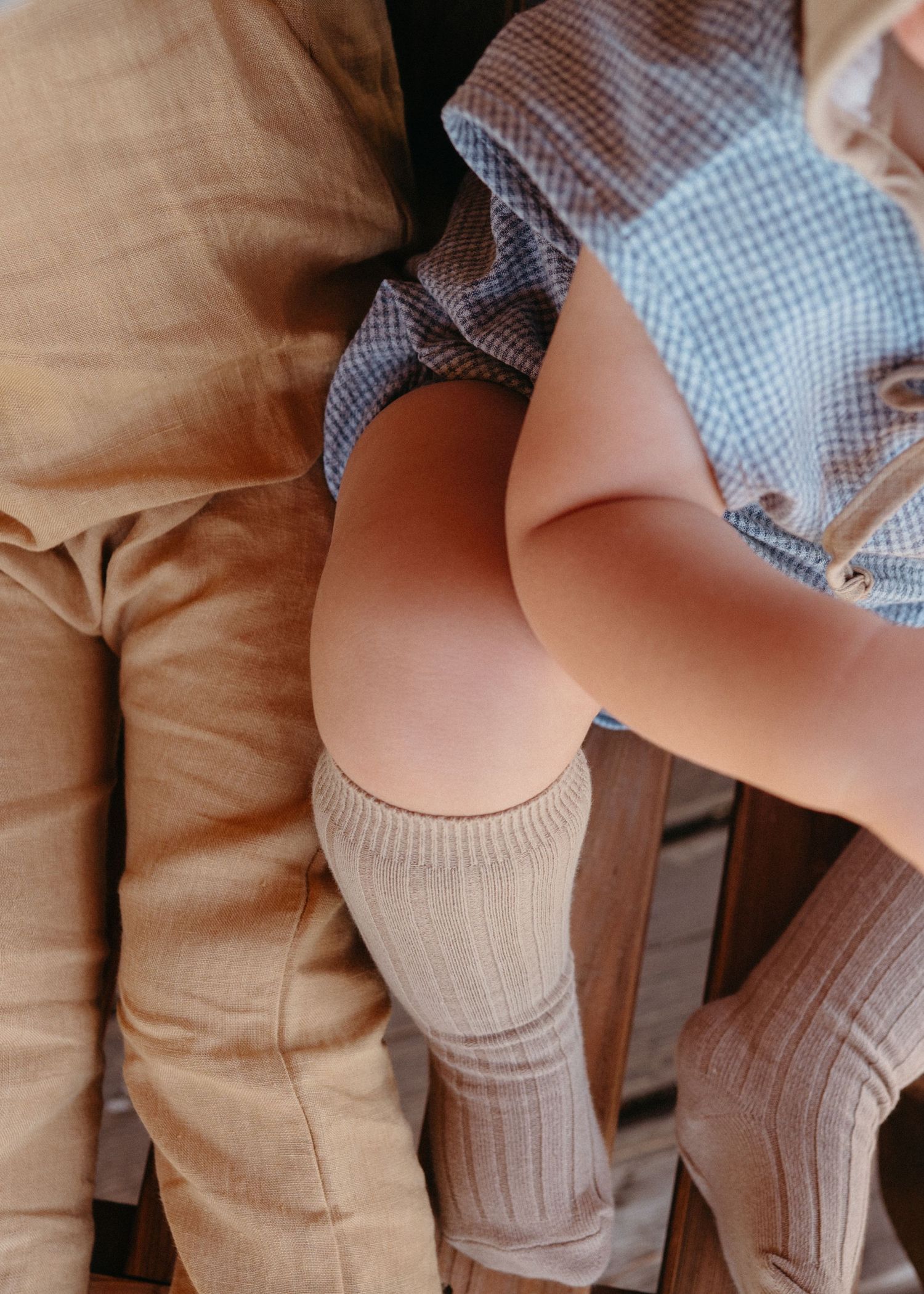 Close-up of a child wearing knee-high socks and gingham outfit seated on a wooden chair.